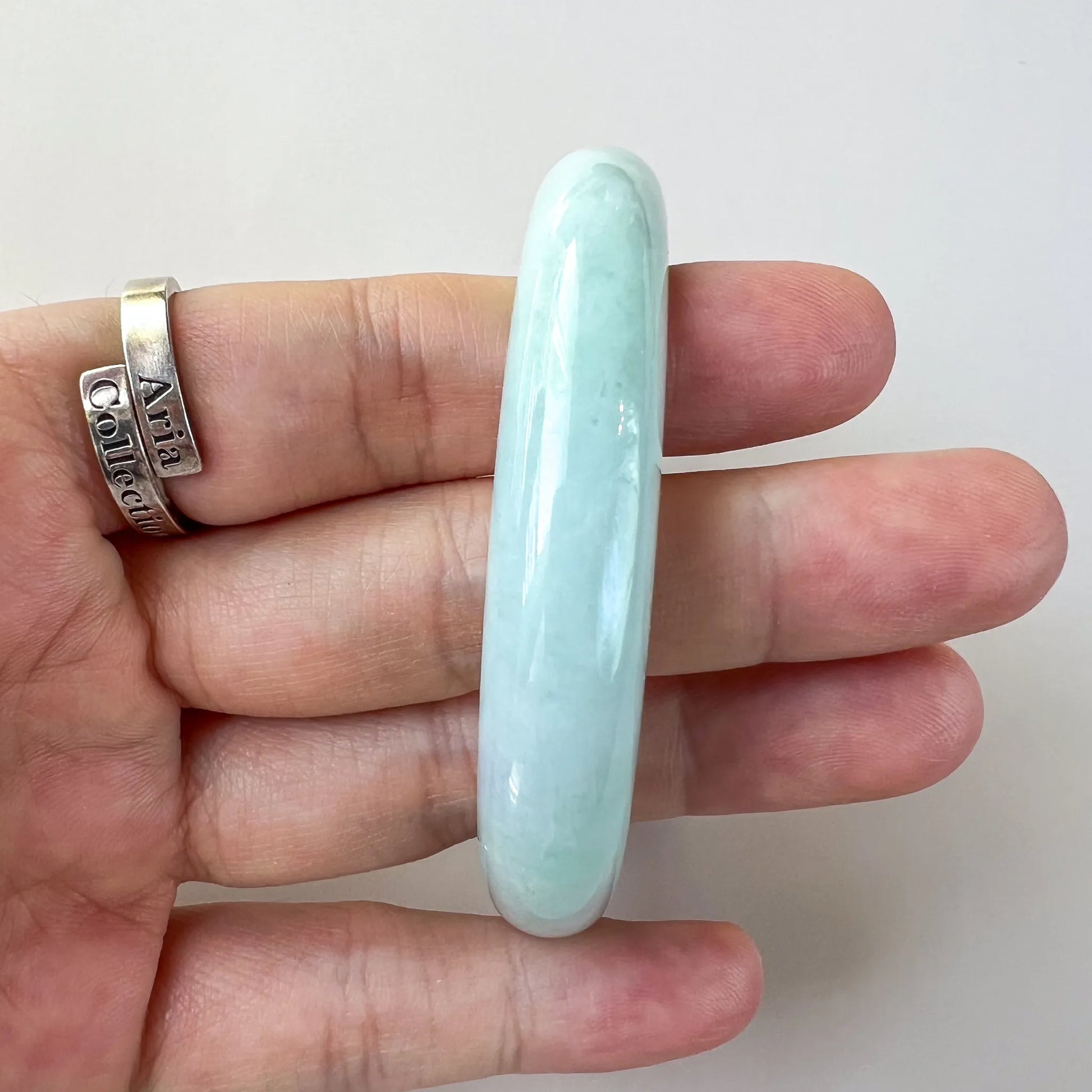 Slim side view of glossy pale blue jade bangle held in hand, rounded edges