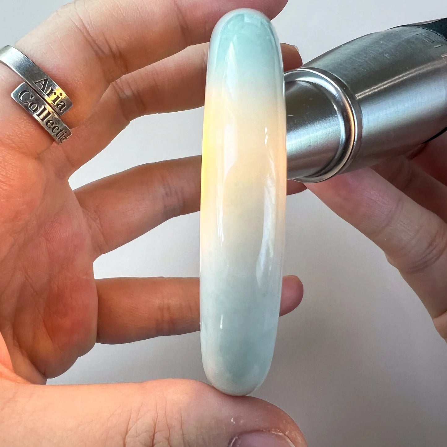 Side view of polished jade bangle under bright light, showing soft color gradient