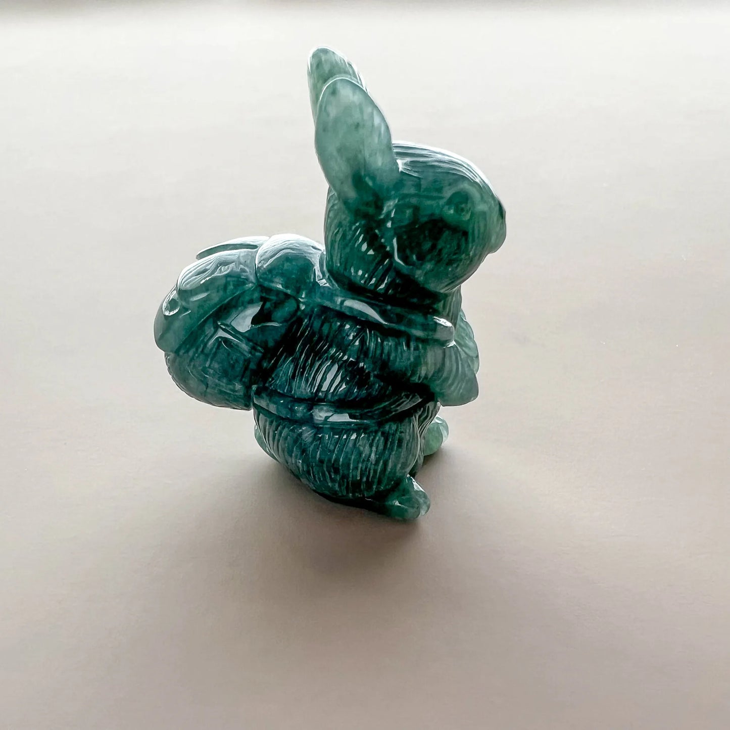 Rear three-quarter view of green carved stone rabbit sculpture with polished finish