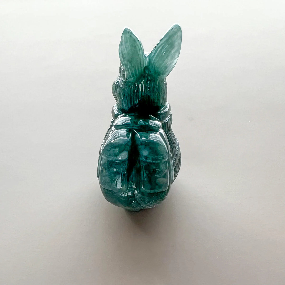 Back view of translucent green carved rabbit figurine with glossy polished stone finish