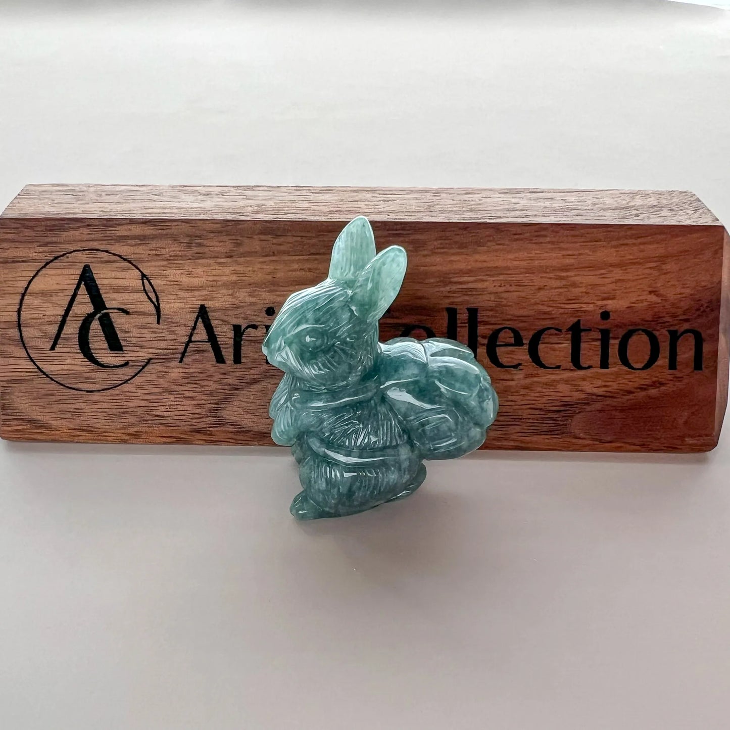 Side view of green carved rabbit sculpture displayed on branded wooden block