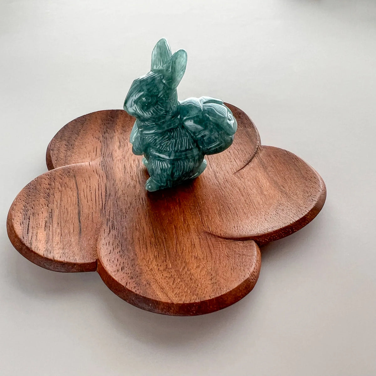 Angled view of green carved rabbit figurine on flower-shaped wooden display base