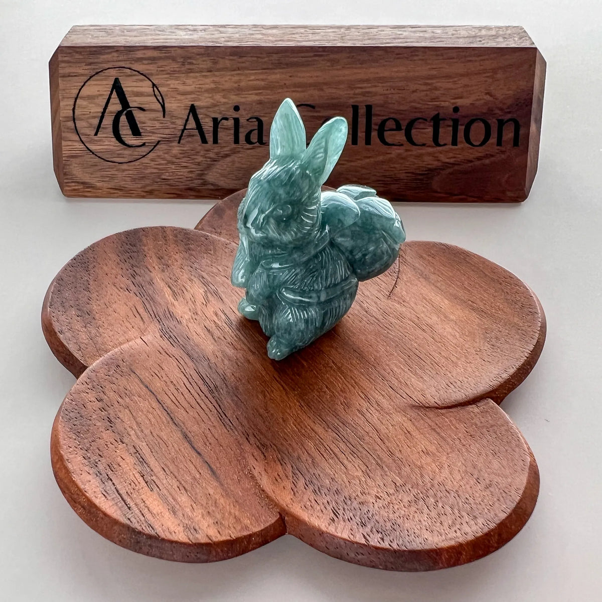 Front angled view of green stone rabbit sculpture with branded wooden display block