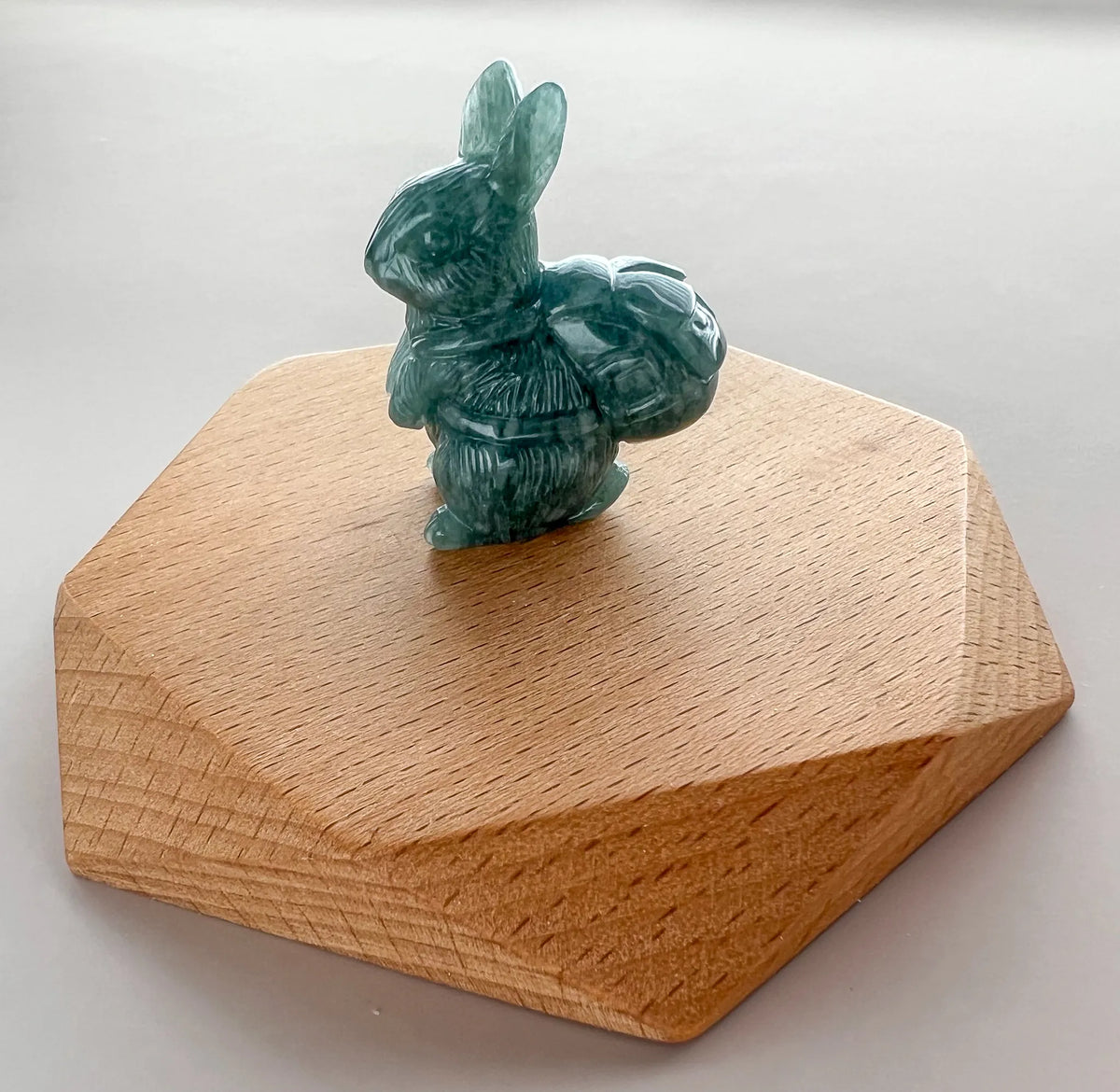 Green carved rabbit figurine on faceted wooden base, shown in angled studio view