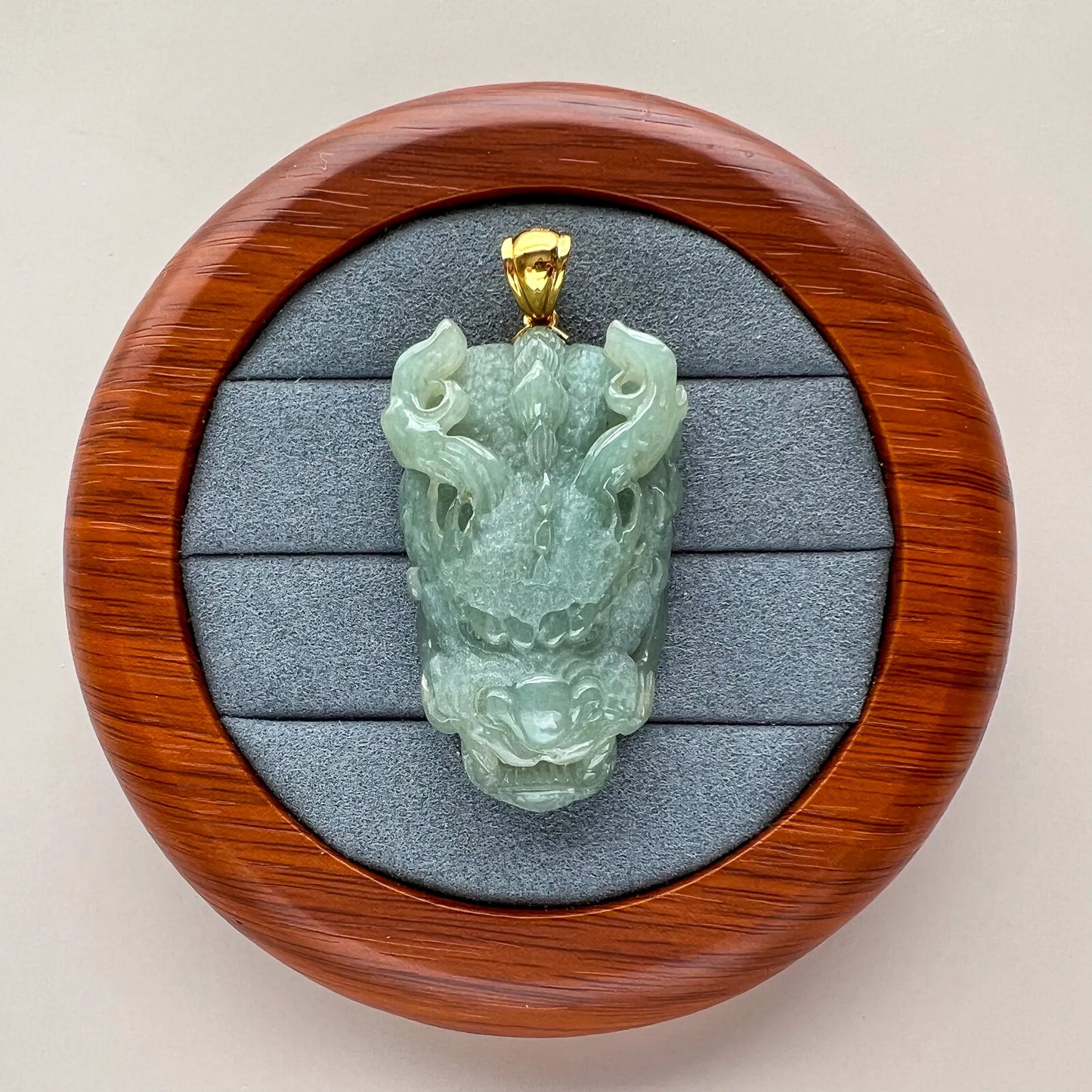 Front view of carved green jade pendant in a wooden presentation box