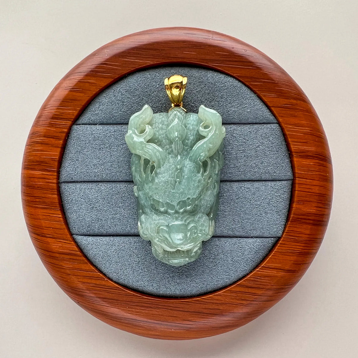 Front view of carved green jade pendant in a wooden presentation box