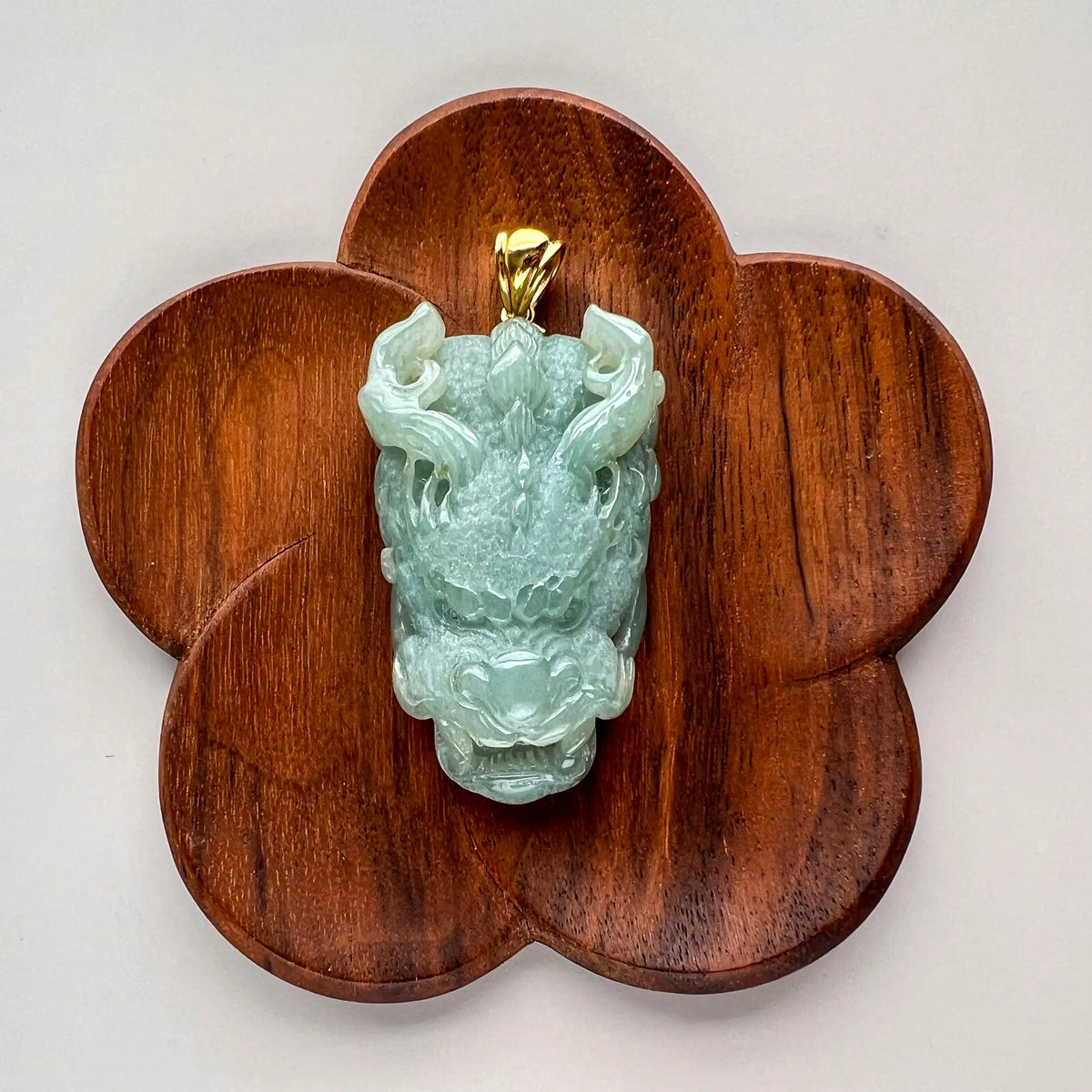 Front view of carved green jade pendant on flower-shaped wooden stand