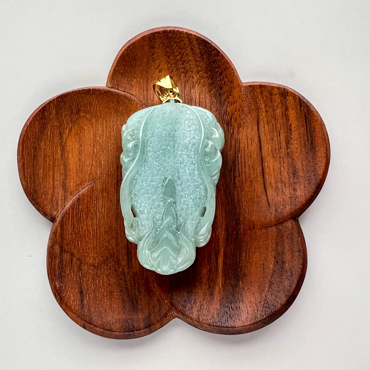 Back view of carved green jade pendant on flower-shaped wooden stand