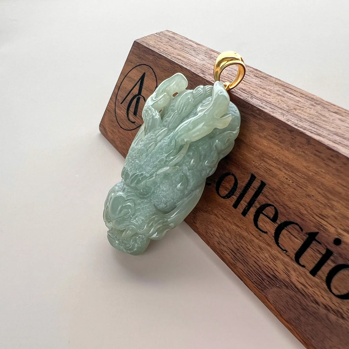 Angled side view of carved green jade dragon pendant with polished gold bail