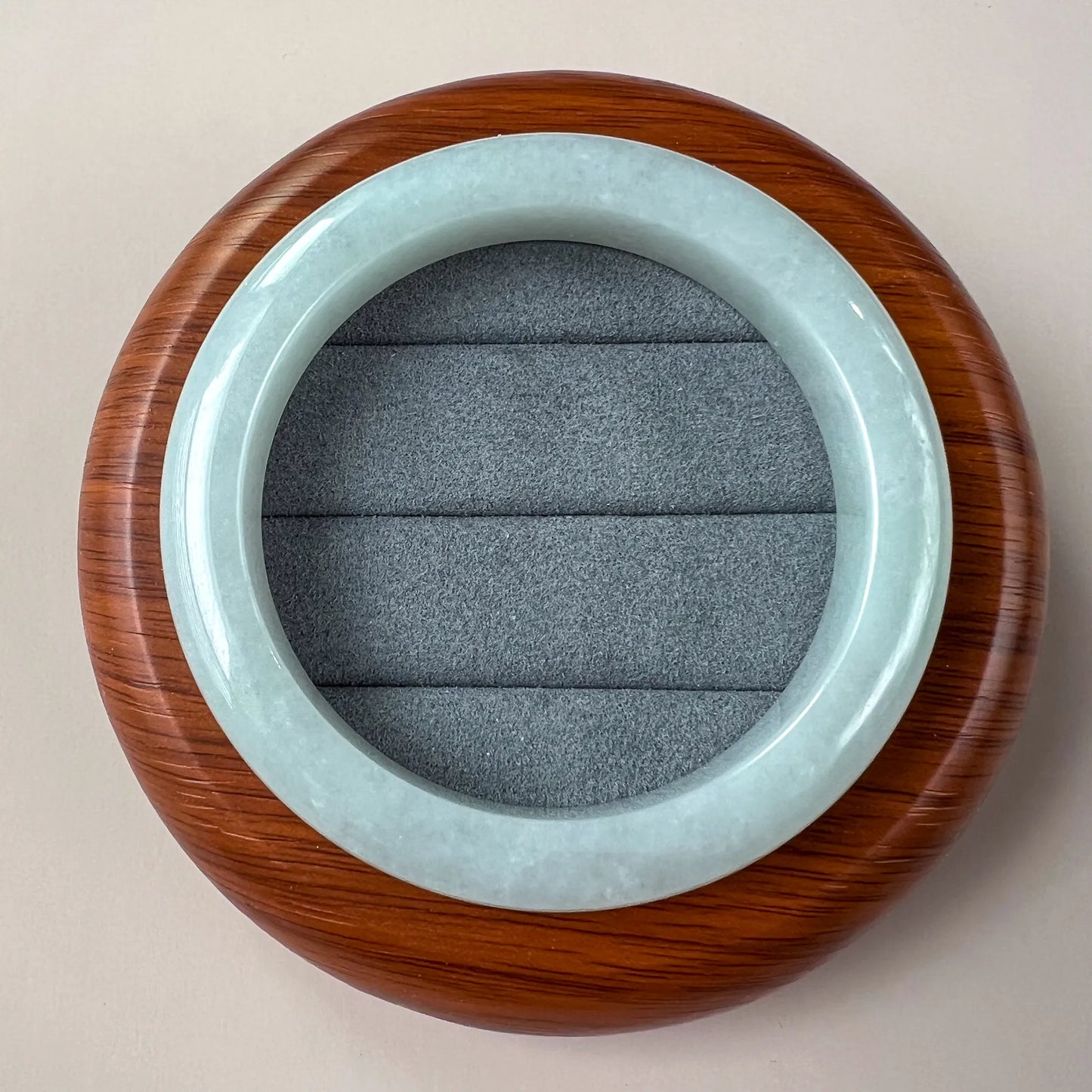 Round jade bangle displayed on wooden stand with gray cushion insert