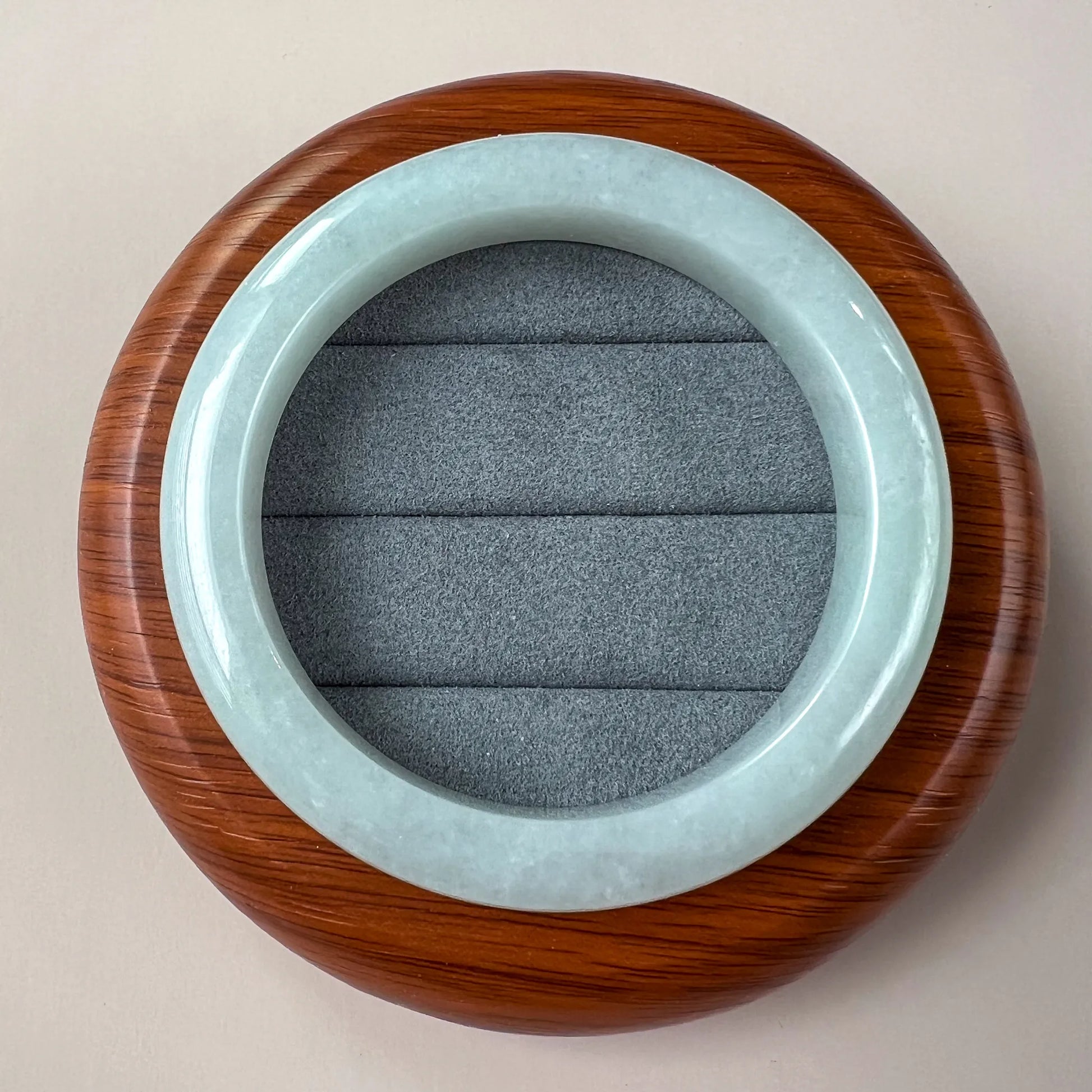 Round jade bangle displayed on wooden stand with gray cushion insert