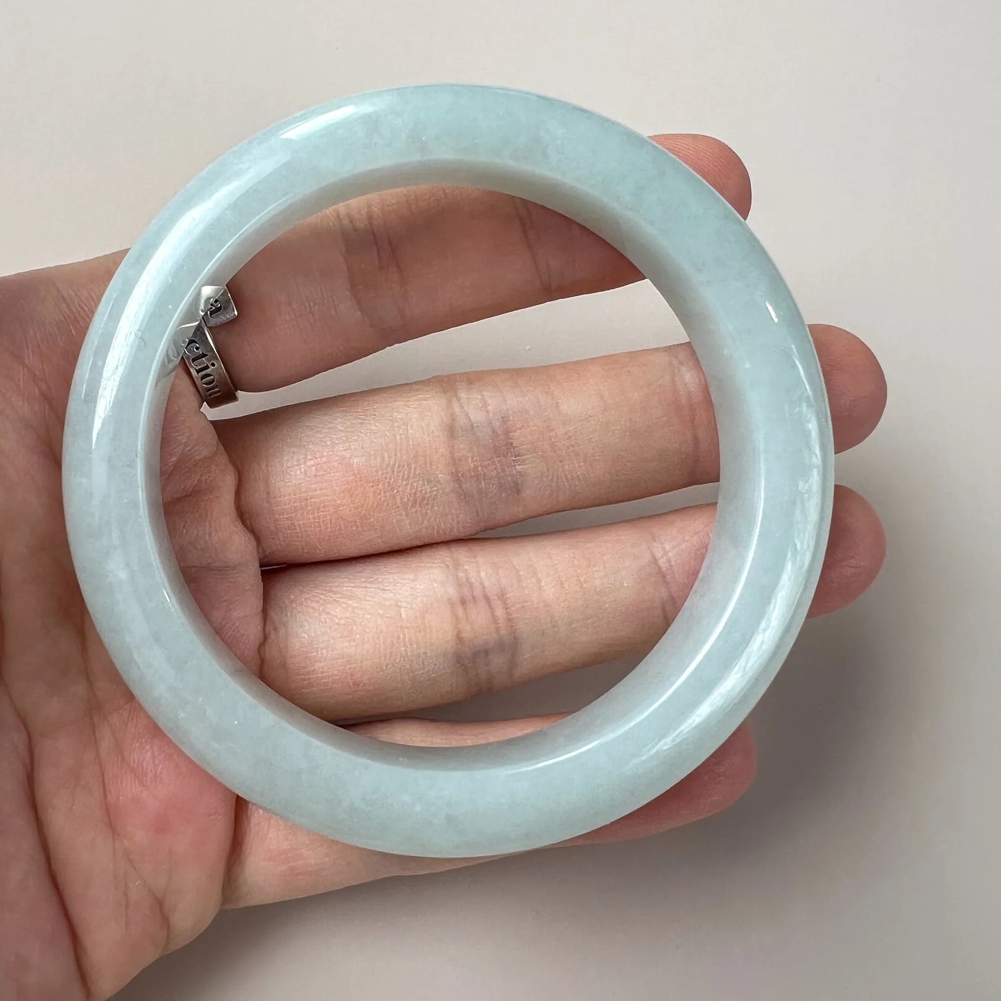 Glossy light blue jade bangle shown on hand for scale