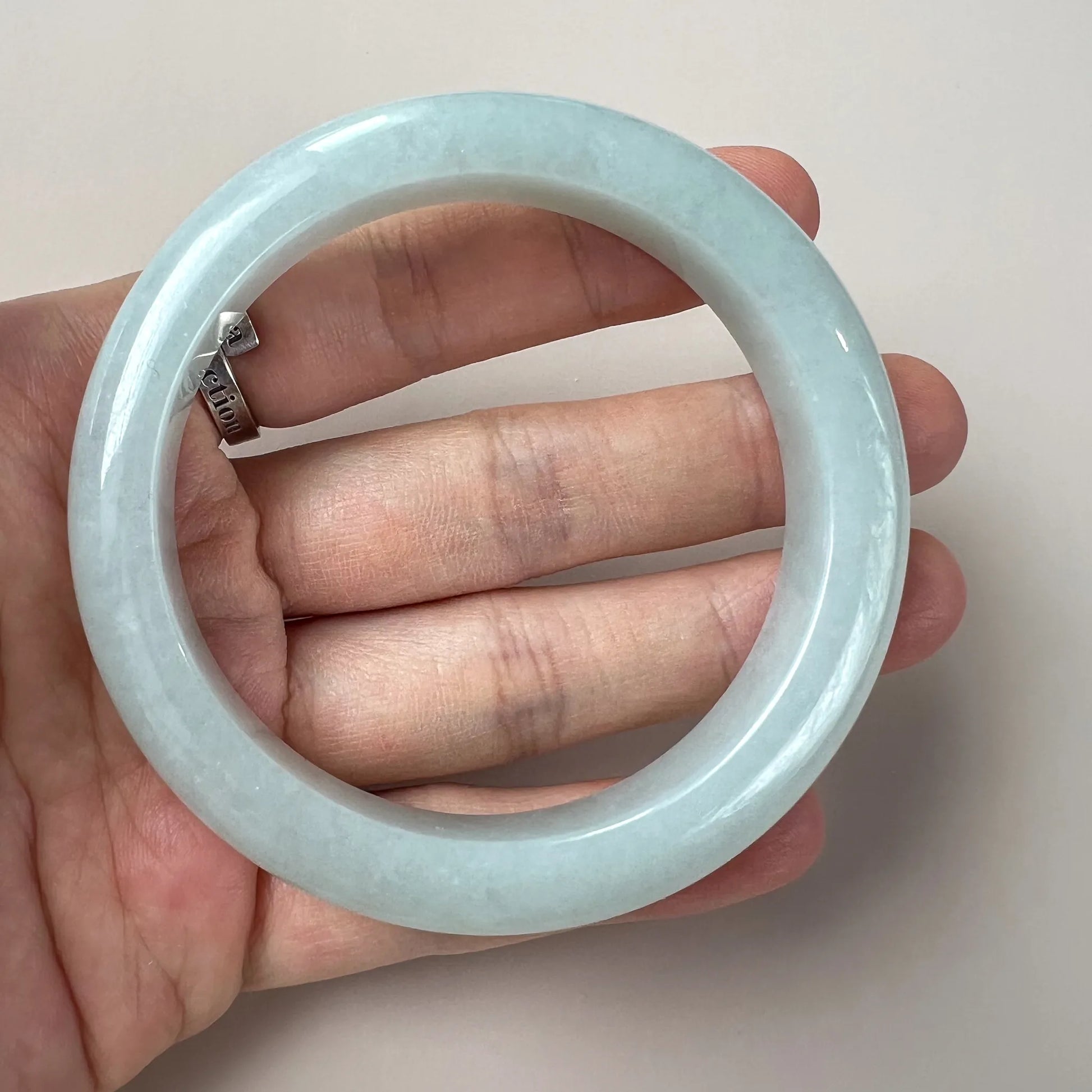 Glossy light blue jade bangle shown on hand for scale