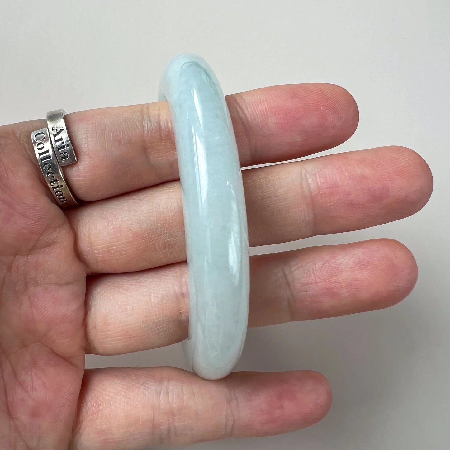 Side profile of polished pale blue jade bangle held between fingers