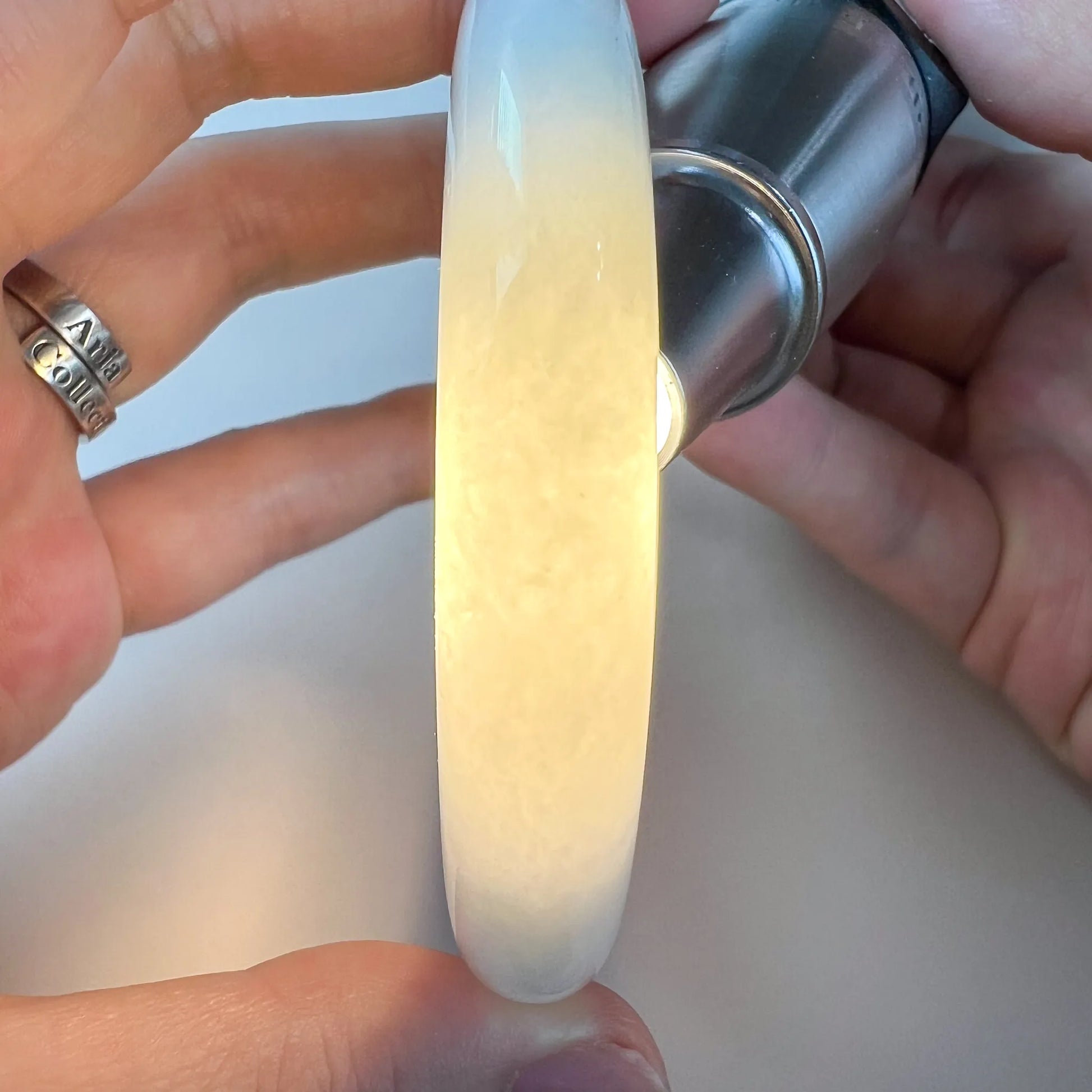 Side profile of translucent light green Natural Jade bangle backlit to show cloudy texture and polished surface