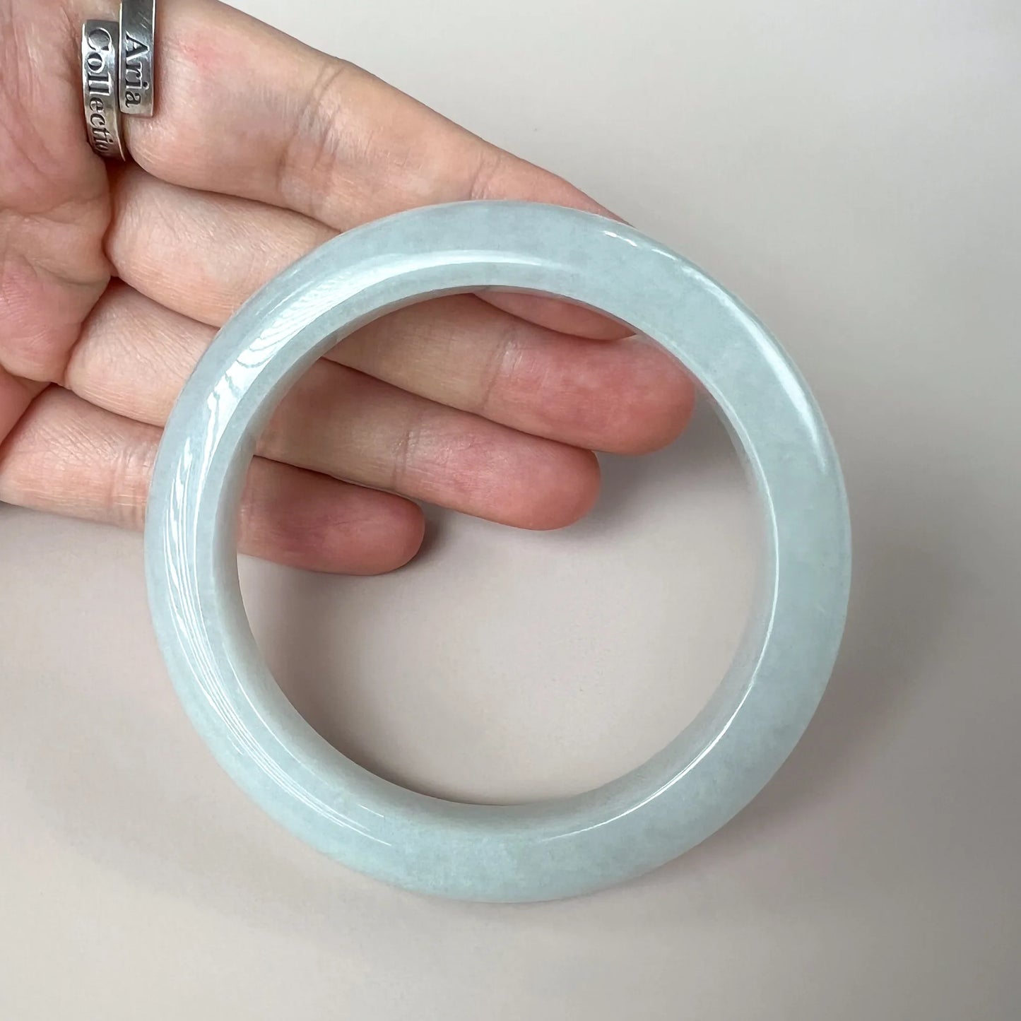 Glossy pale blue jade bangle held in hand, front angle