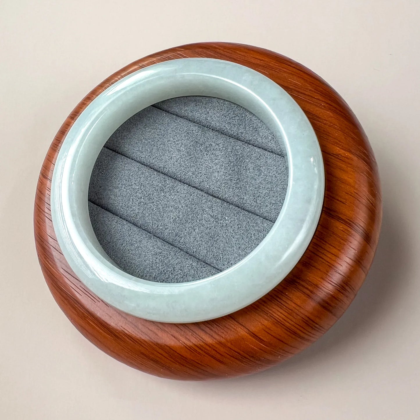 Jade bangle resting on carved wooden display stand with gray insert