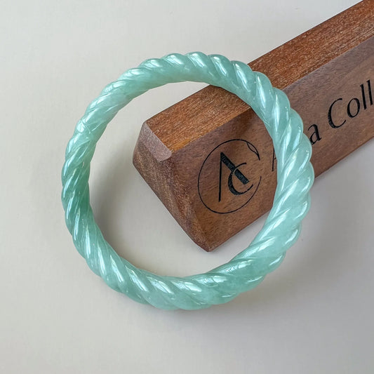 Mint green twisted jade bangle on display stand, polished carved finish, top view