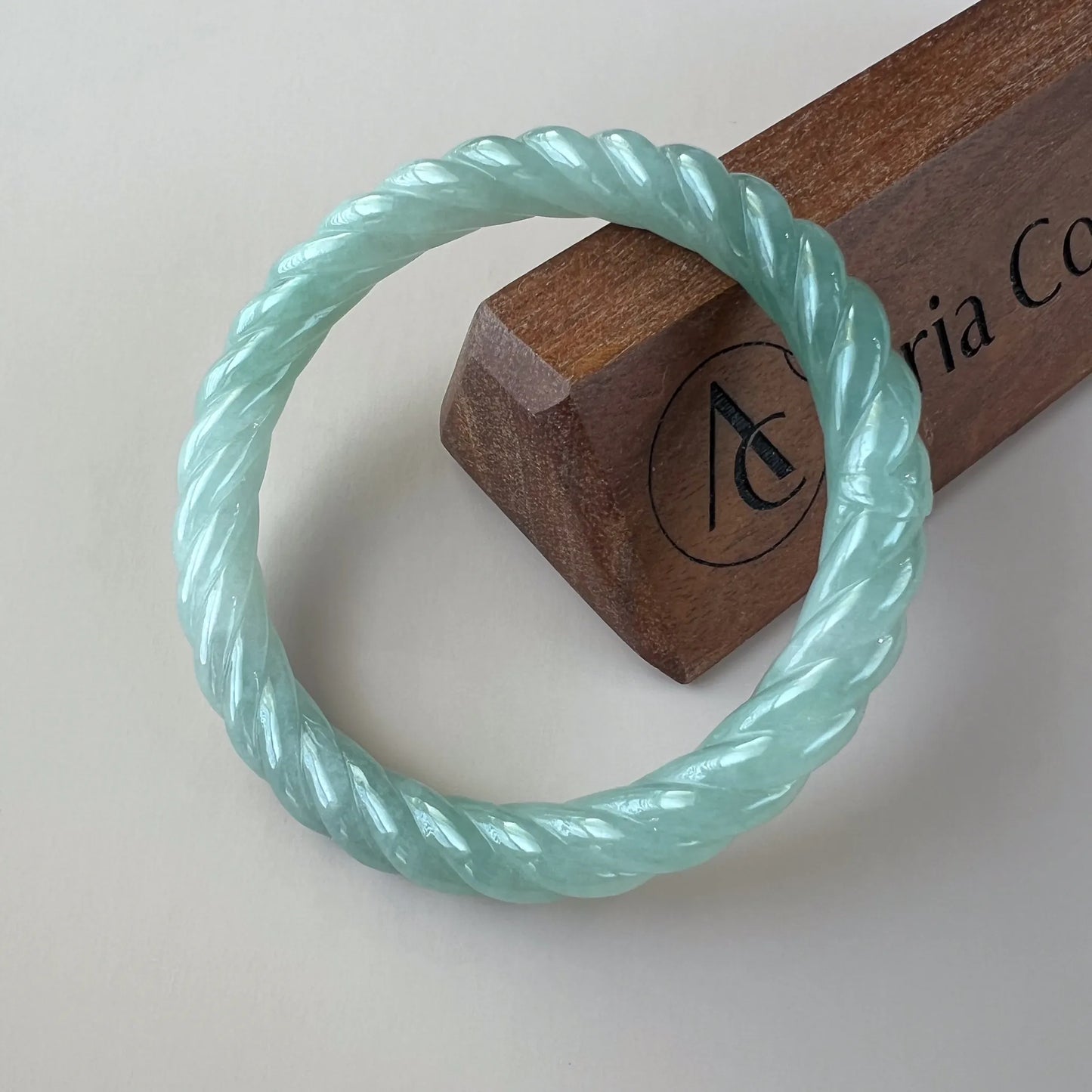 Mint green braided jade bangle, glossy carved surface, angled top view on display stand