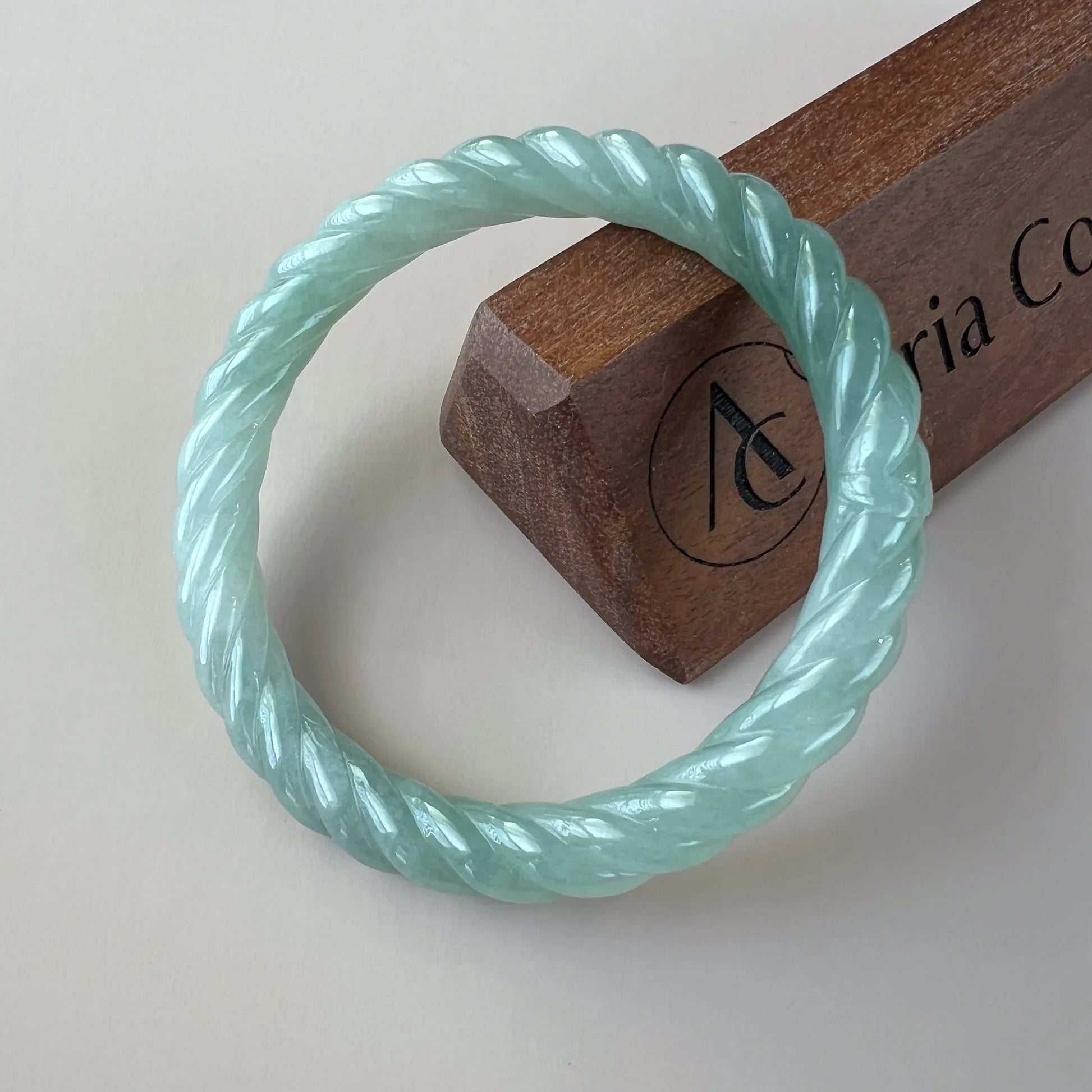 Mint green braided jade bangle, glossy carved surface, angled top view on display stand
