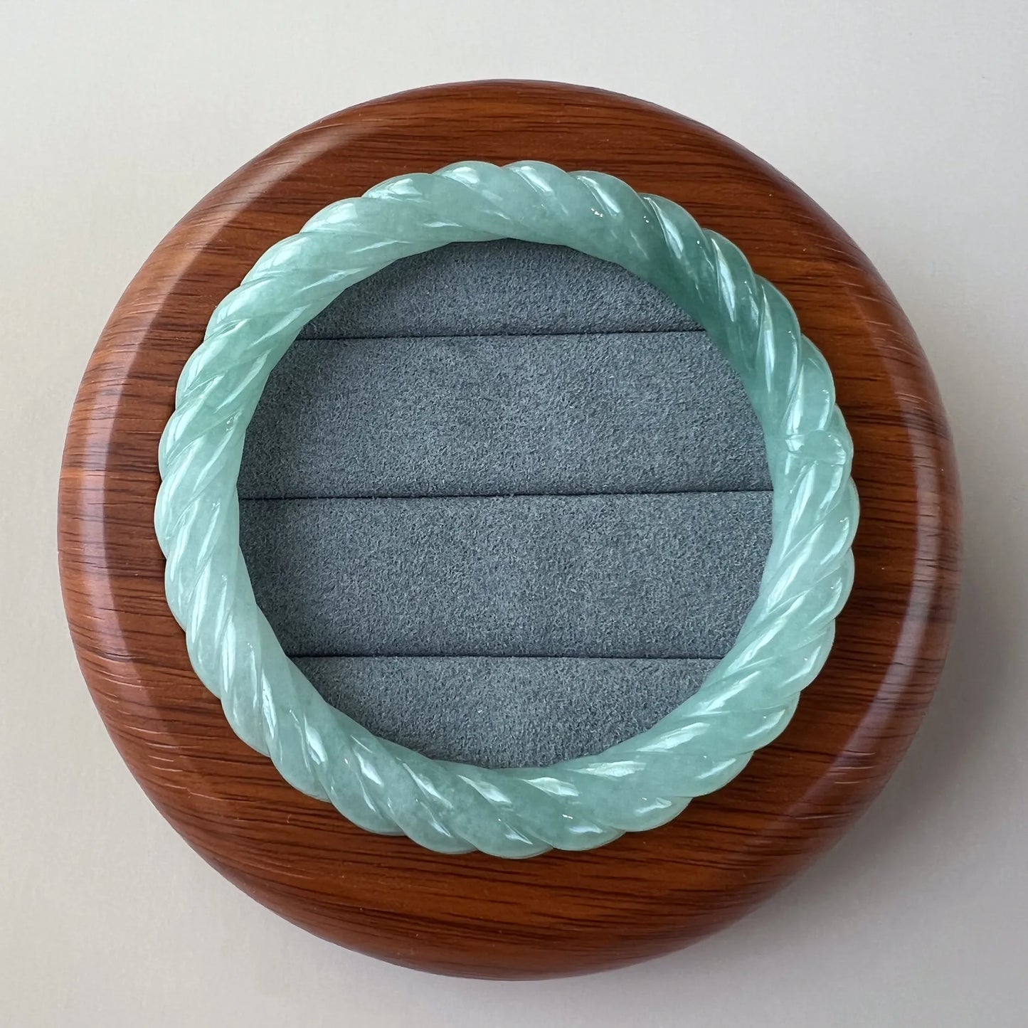 Round twisted jade bangle in wooden display case, polished carved finish, front view