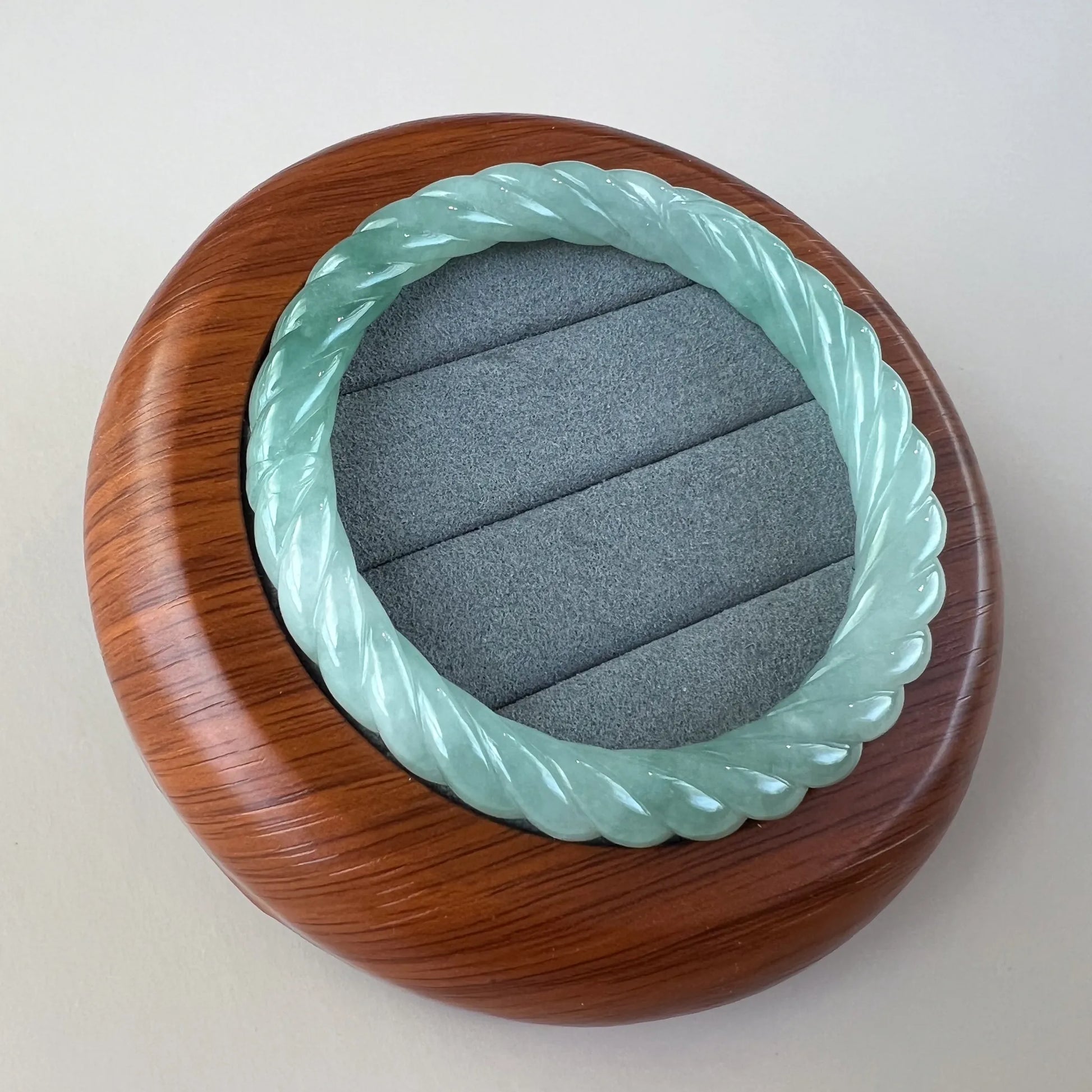 Mint green twisted jade bangle in wooden display case, polished carved finish, angled view