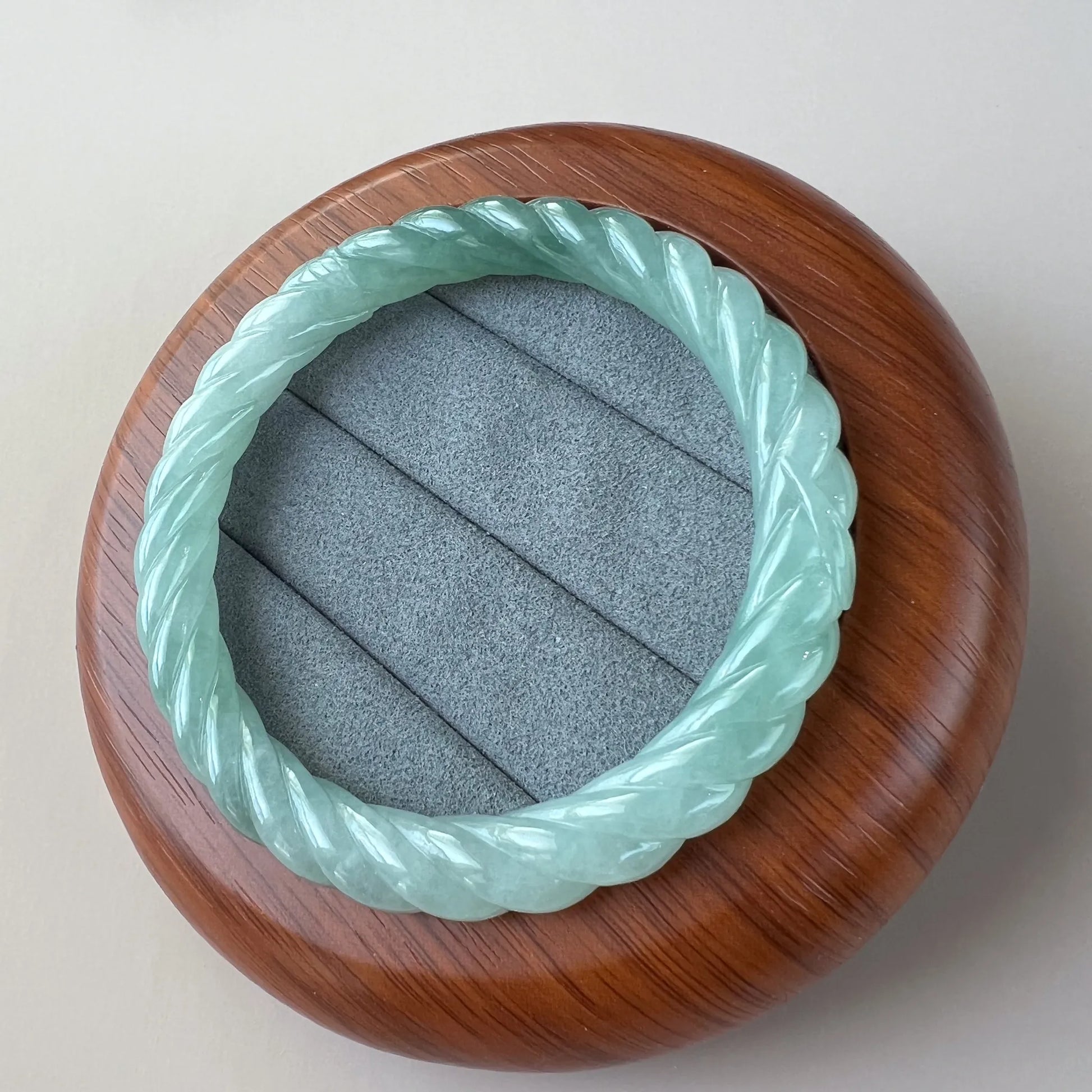 Mint green twisted jade bangle in wooden display case, polished carved finish, close angled view