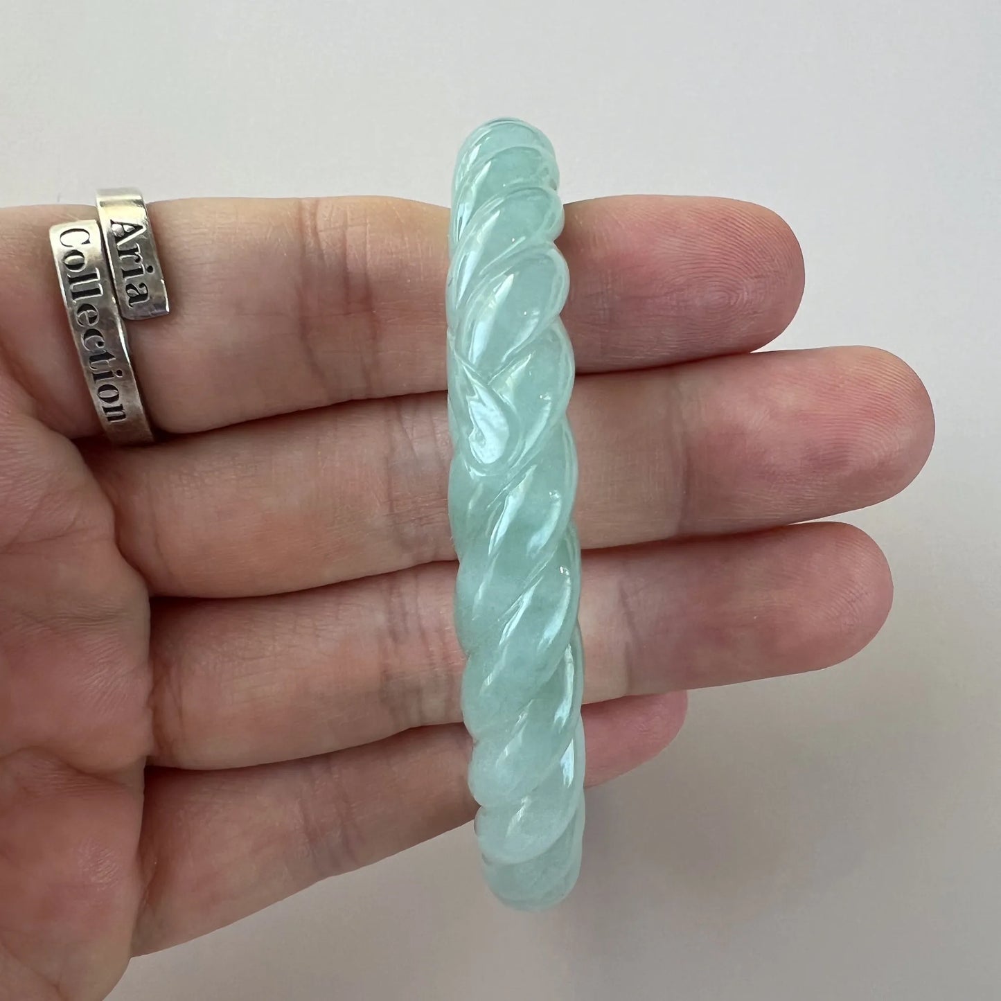 Side profile of mint green twisted jade bangle, polished carved finish, hand-held view