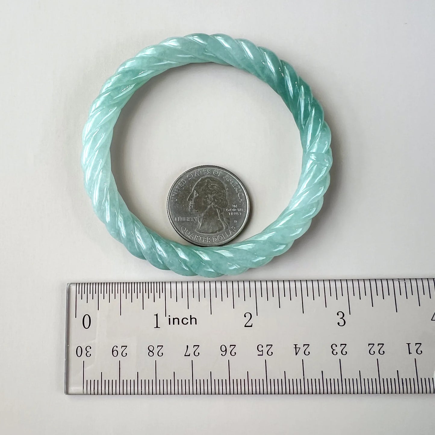 Light blue natural jade bangle shown with ruler and quarter for scale, highlighting carved twisted profile