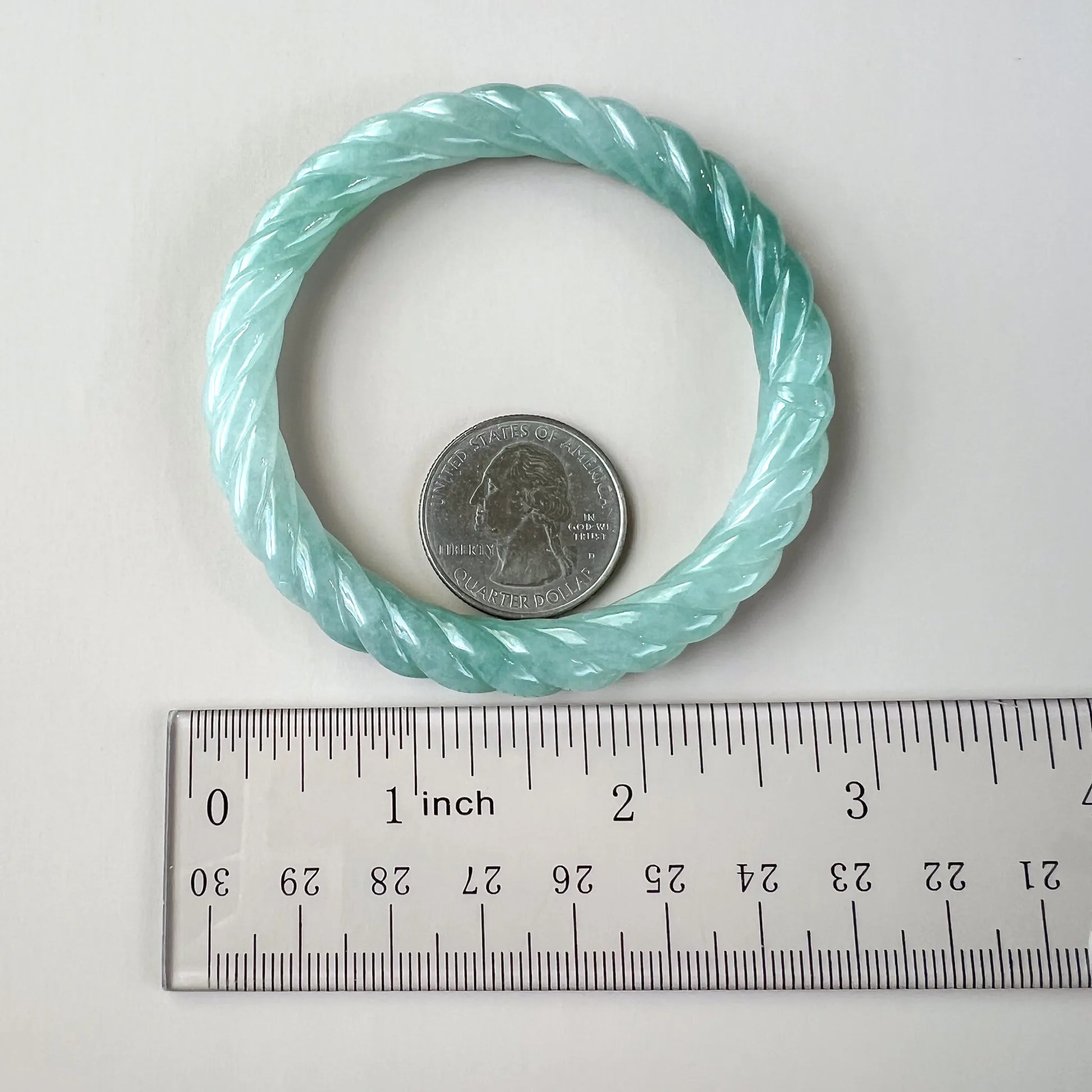 Light blue natural jade bangle shown with ruler and quarter for scale, highlighting carved twisted profile