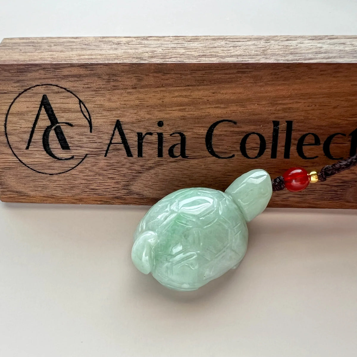 Front view of carved pale green jade turtle pendant with red bead cord on display