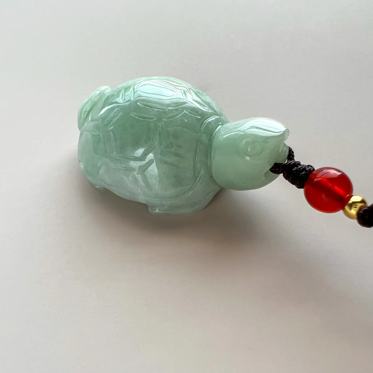 Side view of translucent green jade turtle pendant with polished carved shell detail