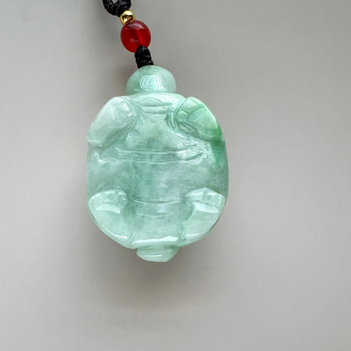 Reverse of light green jade dragon turtle pendant showing carved body details and cord attachment