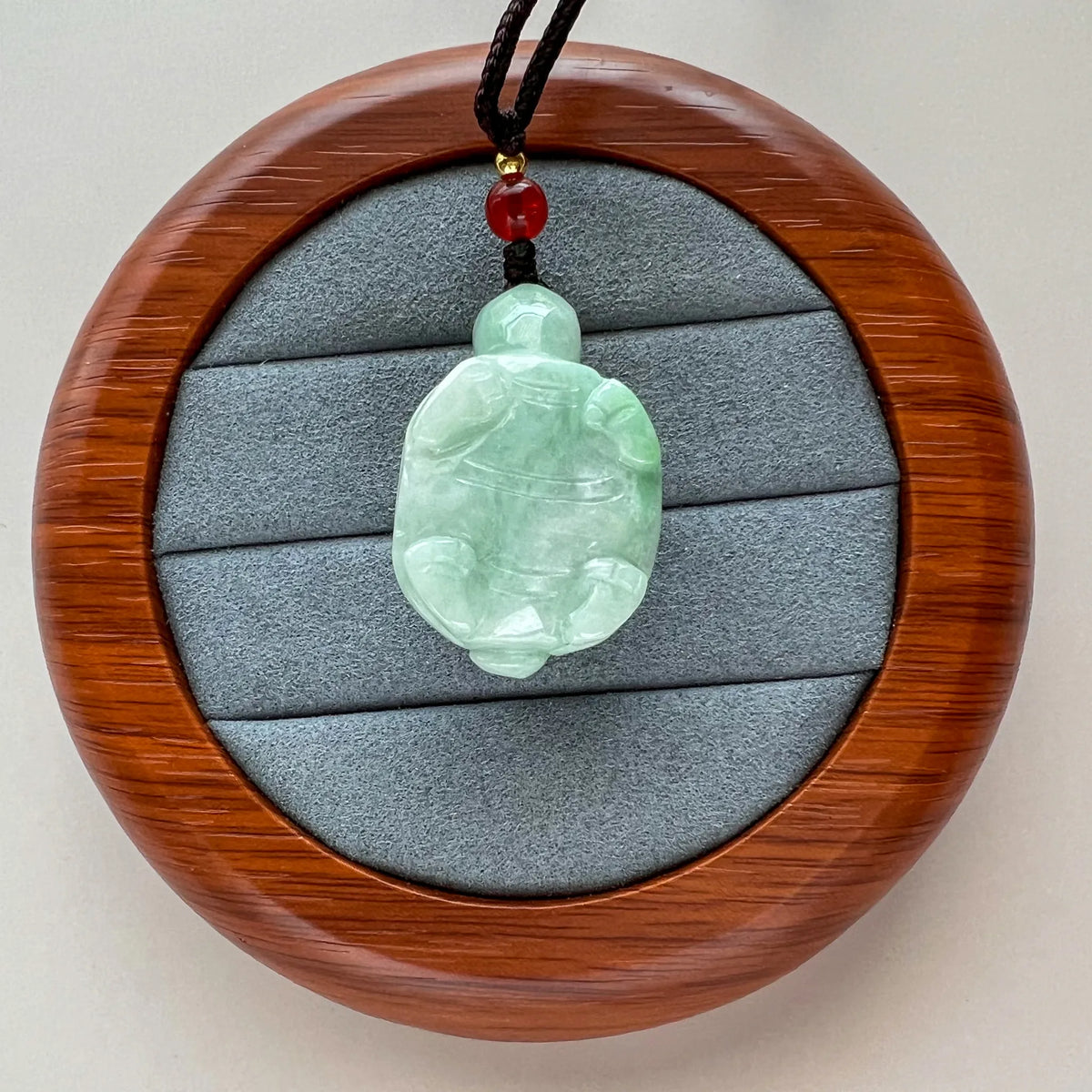 Back view of carved jade turtle pendant in wooden case with braided cord