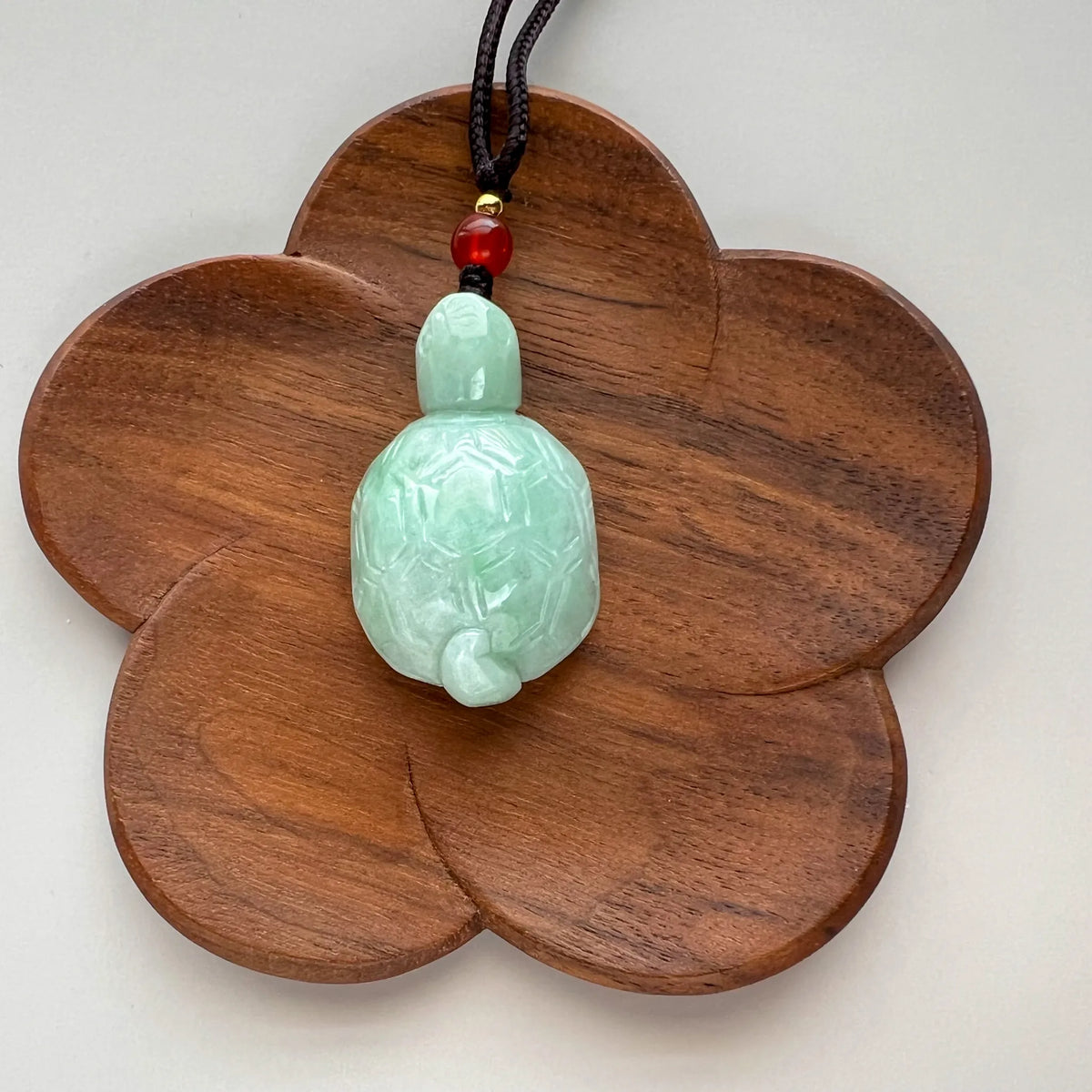 Front view of green jade turtle pendant displayed on flower-shaped wooden stand