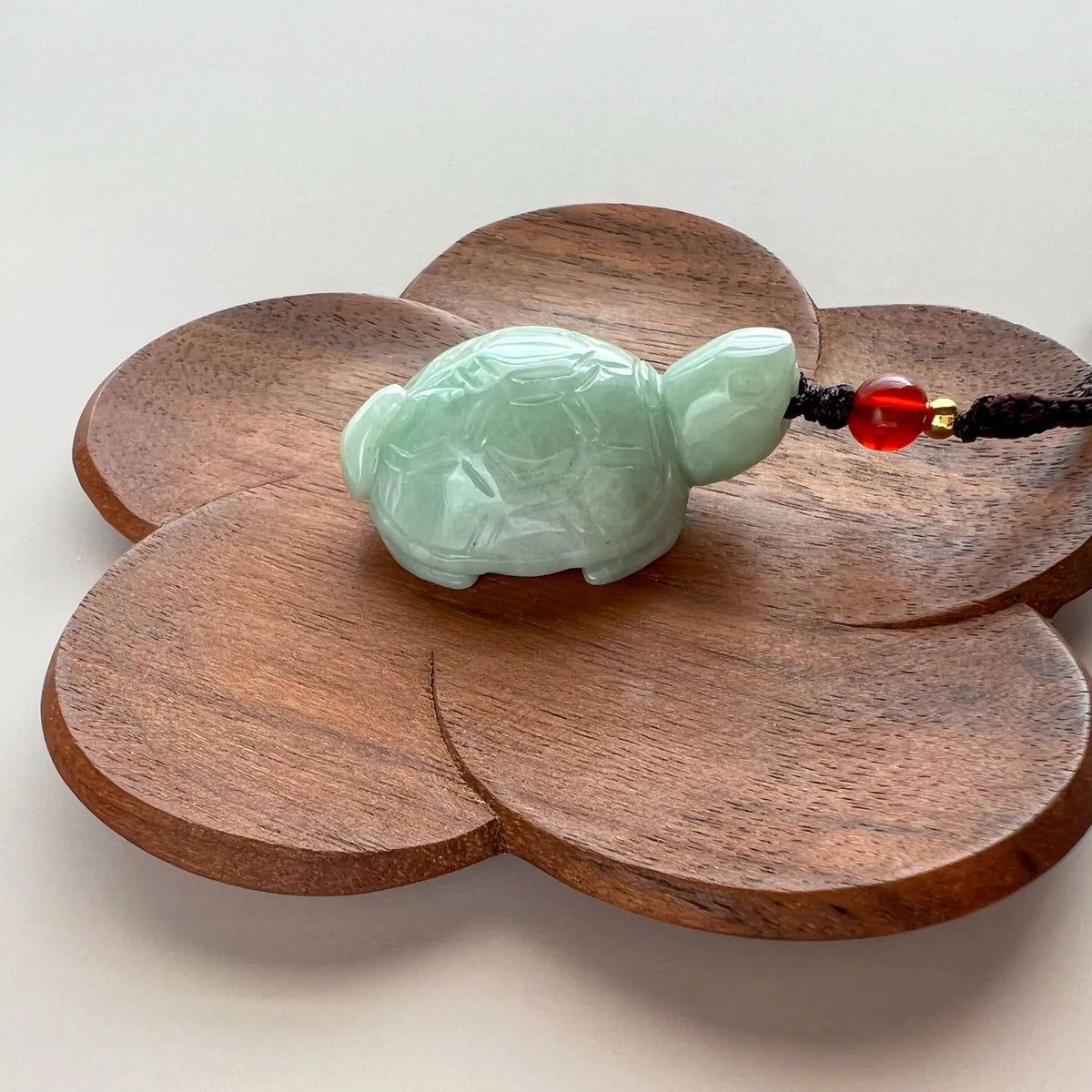 Side profile of translucent jade turtle pendant on carved wooden flower display