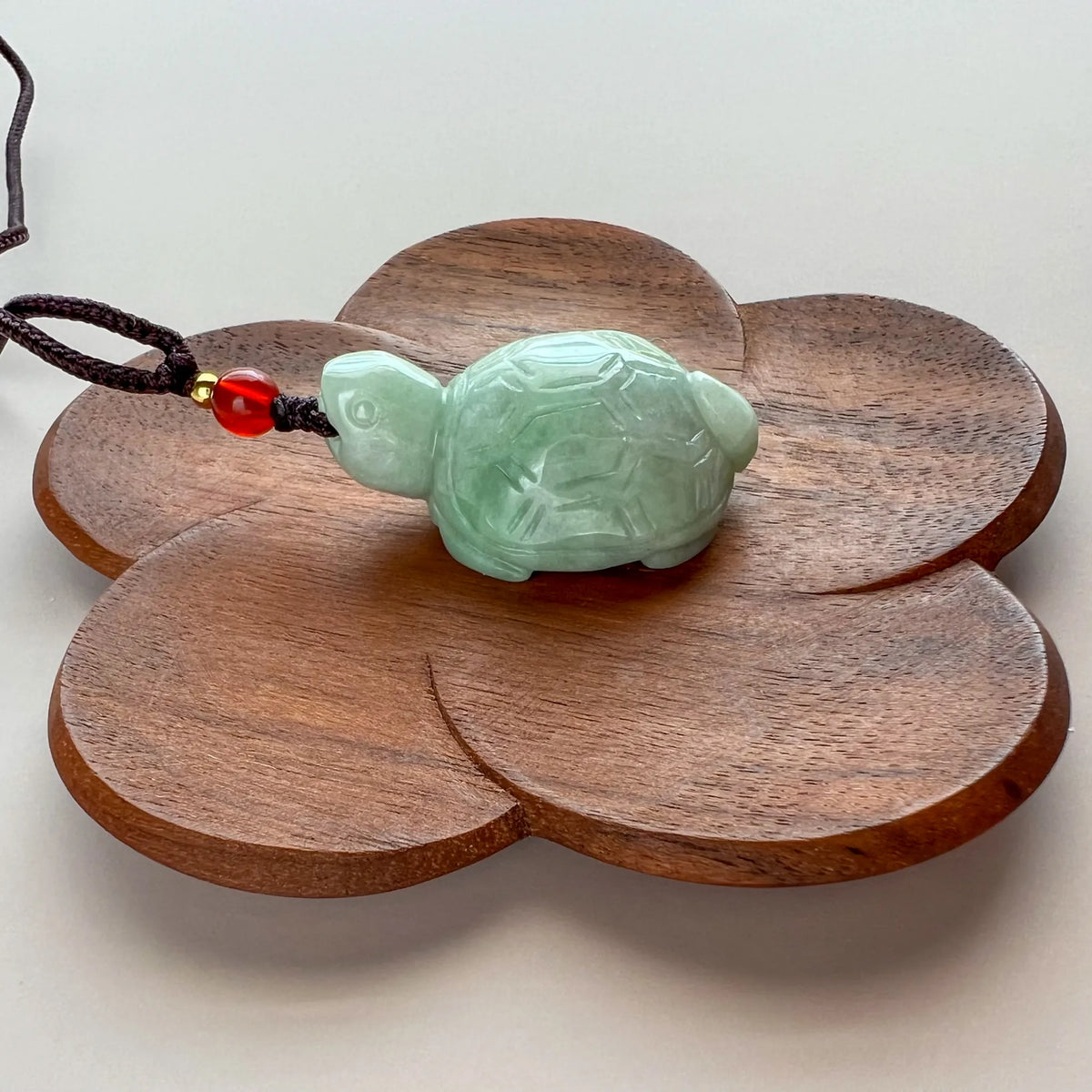 Angled side view of jade turtle pendant with red bead accent on wooden stand