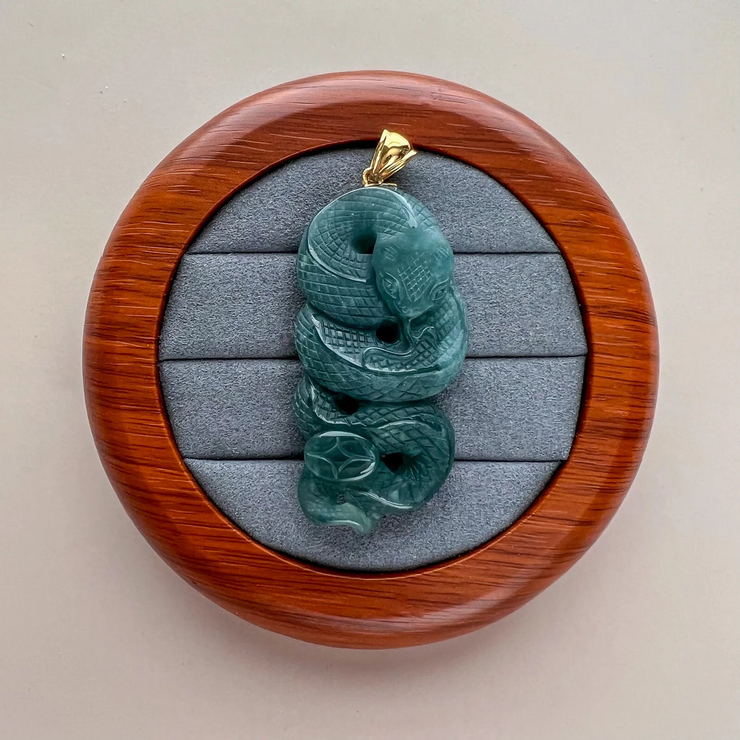 Front view of green carved snake jade pendant in round display case with gold bail