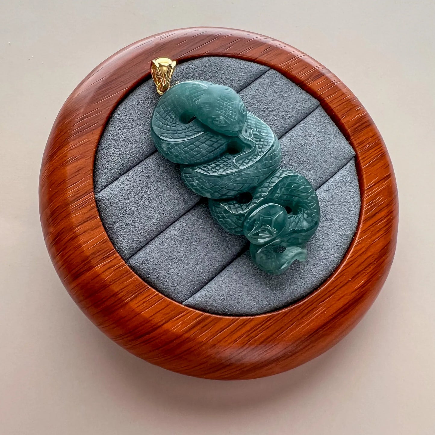 Angled view of carved green snake jade pendant resting in round wooden case