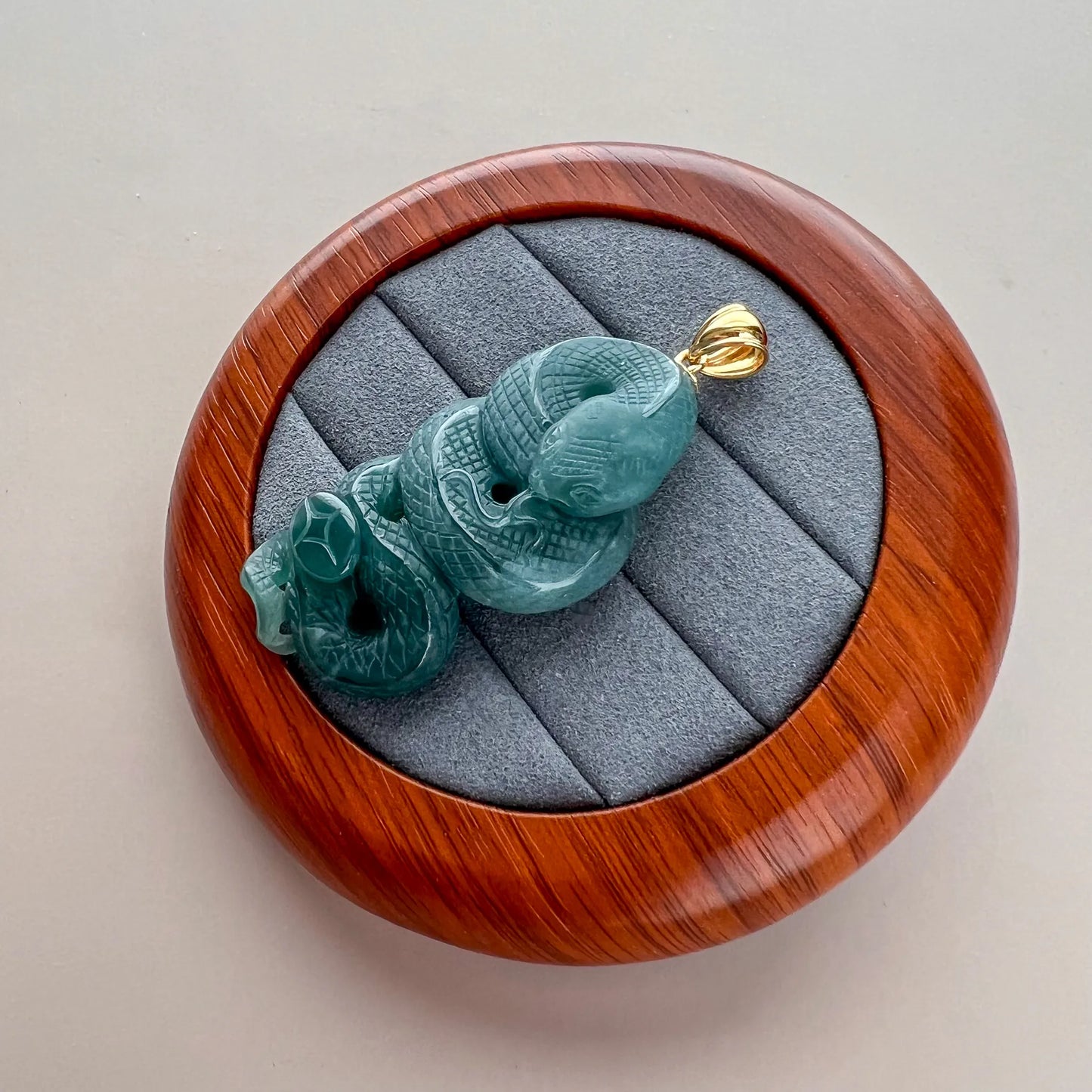 Side-angled view of green carved snake jade pendant with gold bail on padded case