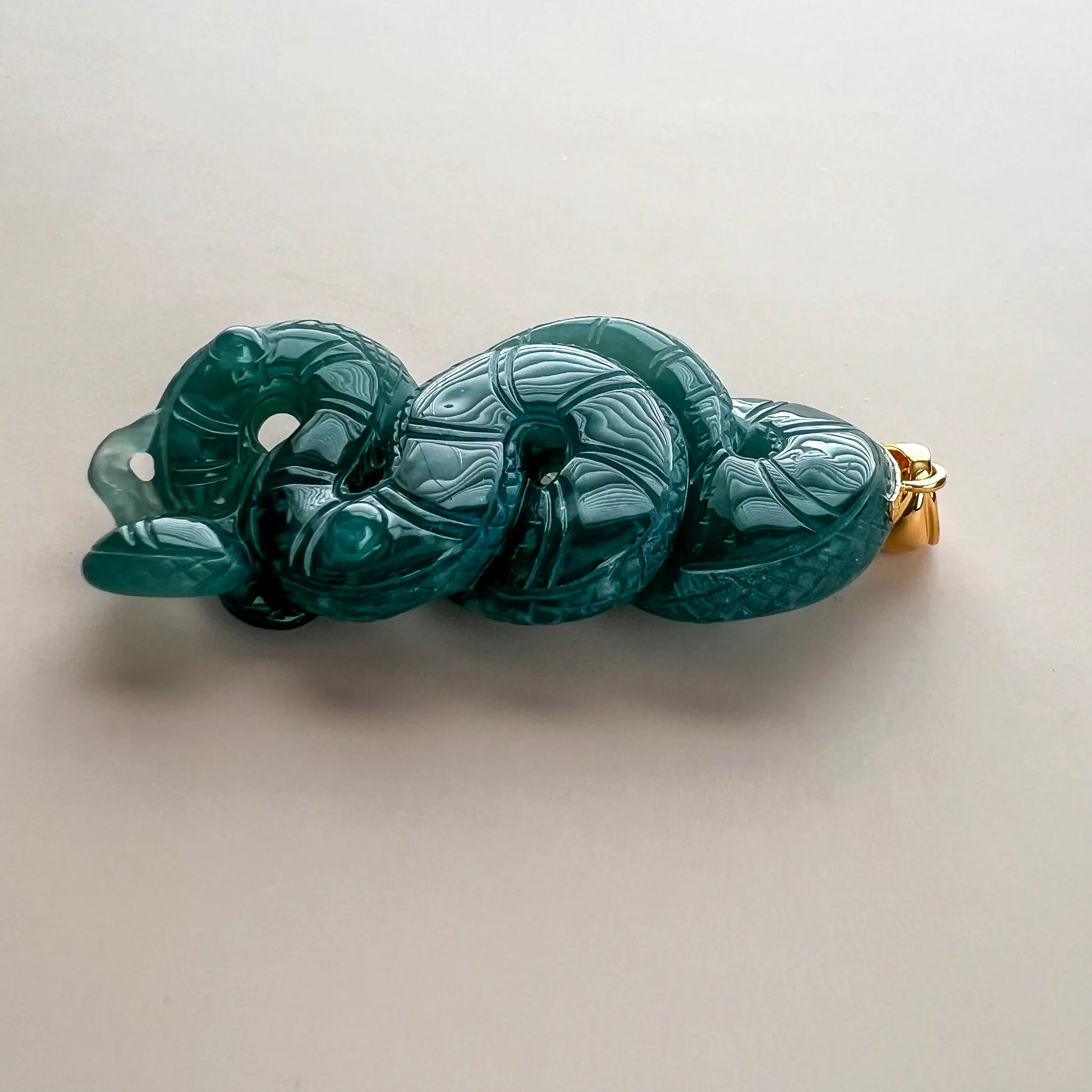 Side profile of carved green jade snake pendant showing layered body and polished finish