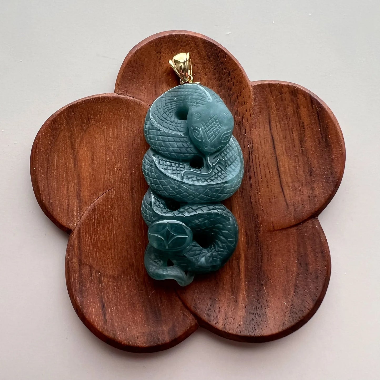 Green carved snake jade pendant displayed on flower-shaped wooden stand