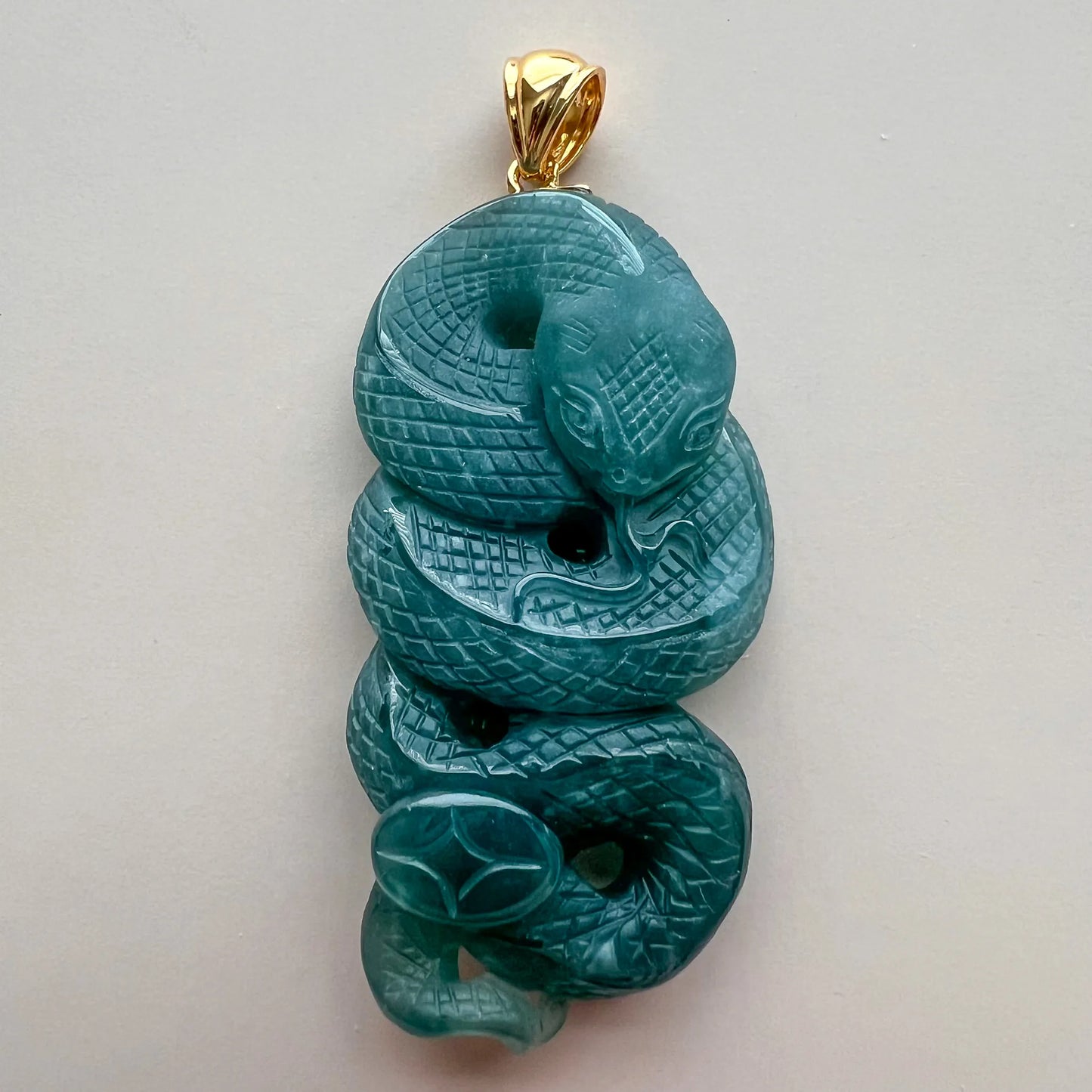 Close front view of polished green snake pendant with detailed scale carving and gold bail
