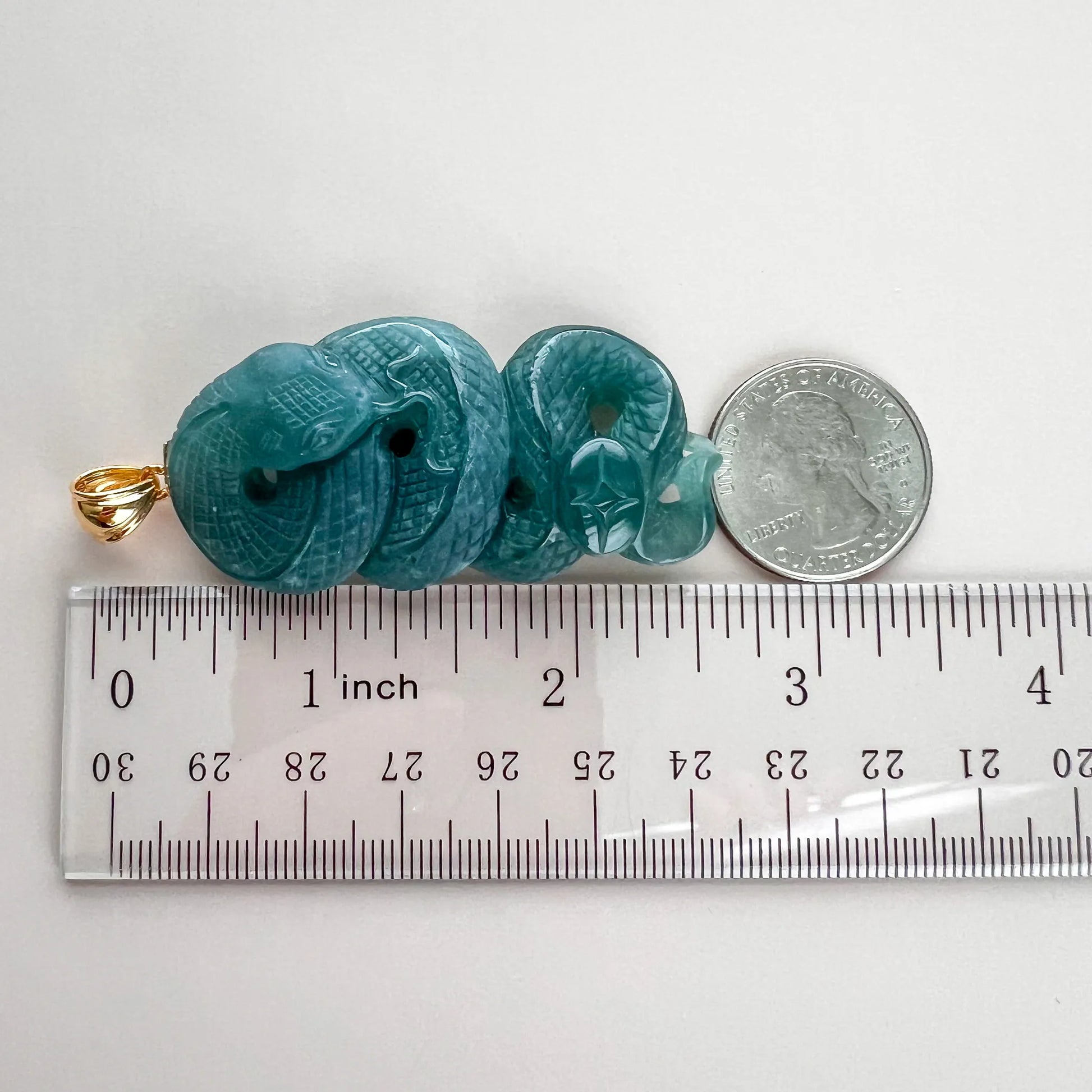Side view of green jade snake pendant beside ruler and coin for size reference