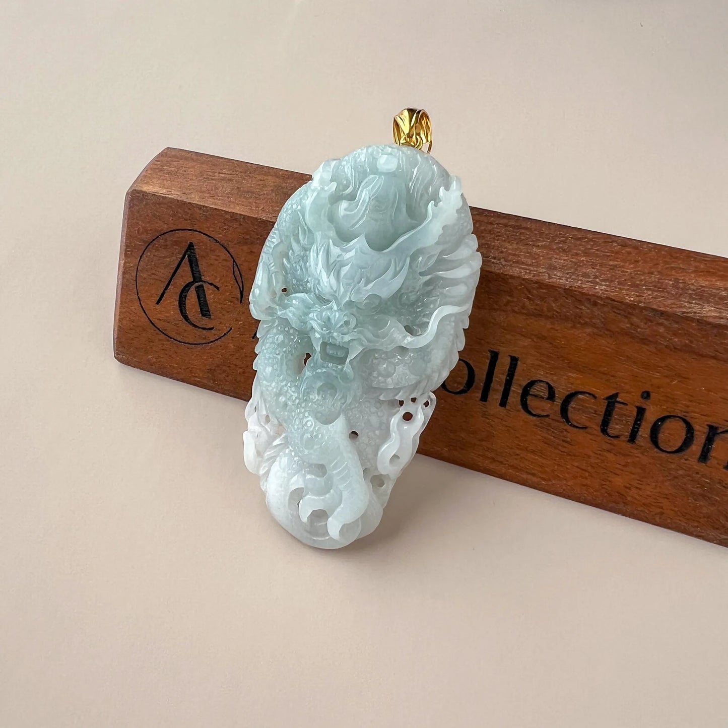 Angled front view of translucent jade pendant with gold bail on branded wood