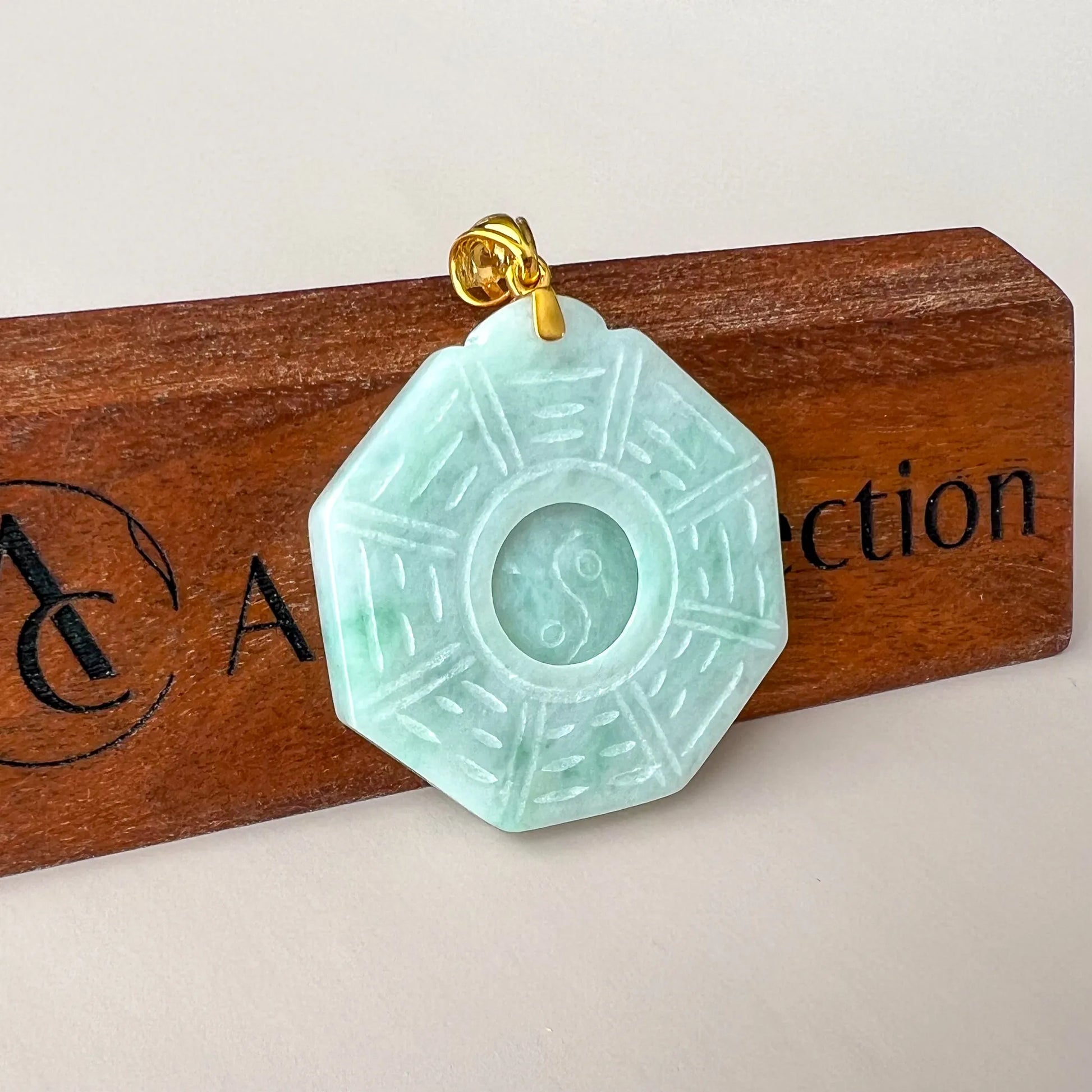 Front view of carved pale green jade pendant with gold bail on wood display