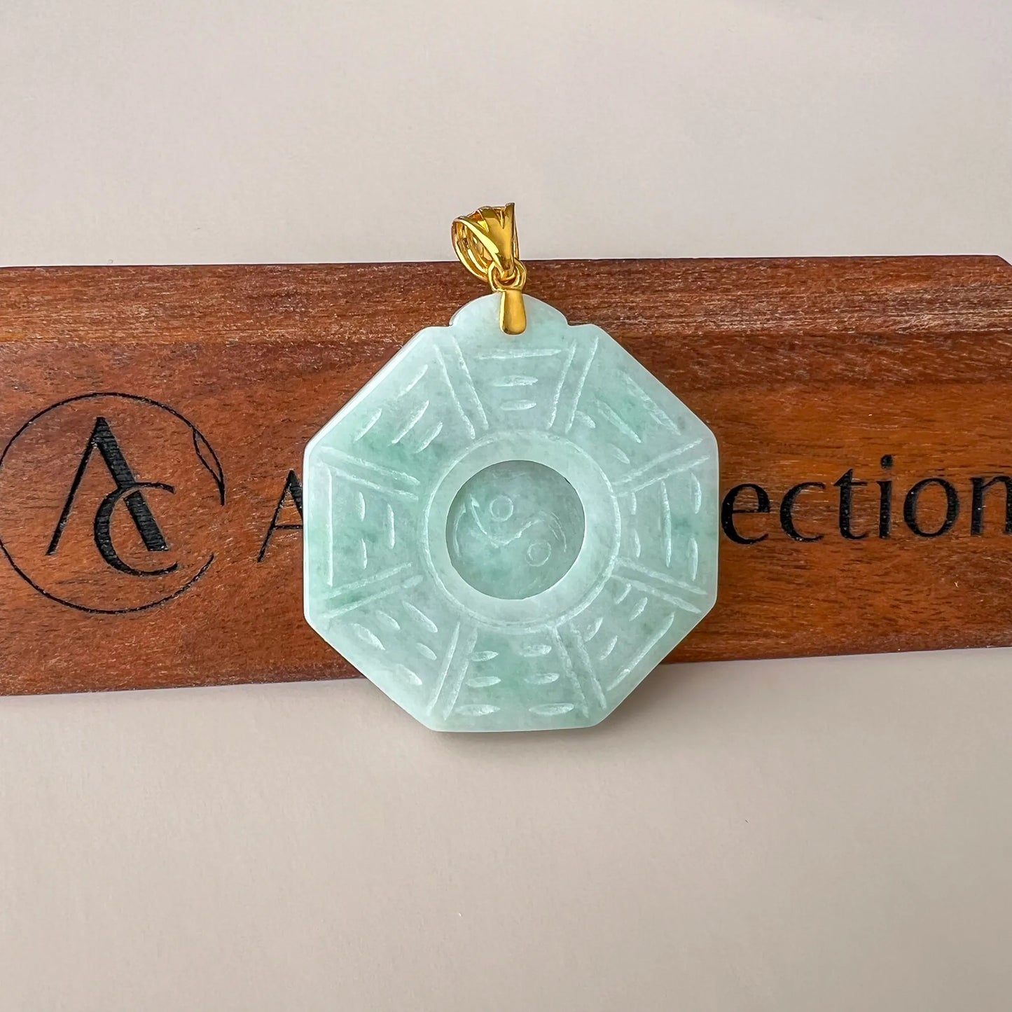 Straight-on view of octagonal jade pendant with engraved symbol details and gold bail