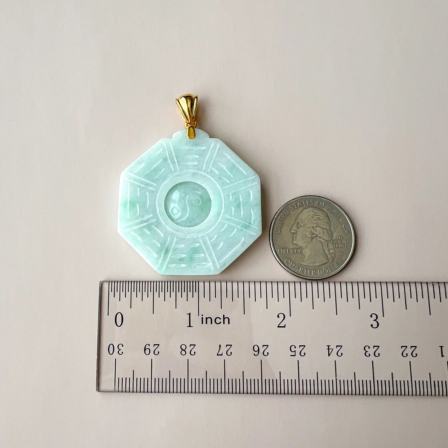 Jade pendant shown with ruler and quarter for size reference on a neutral background