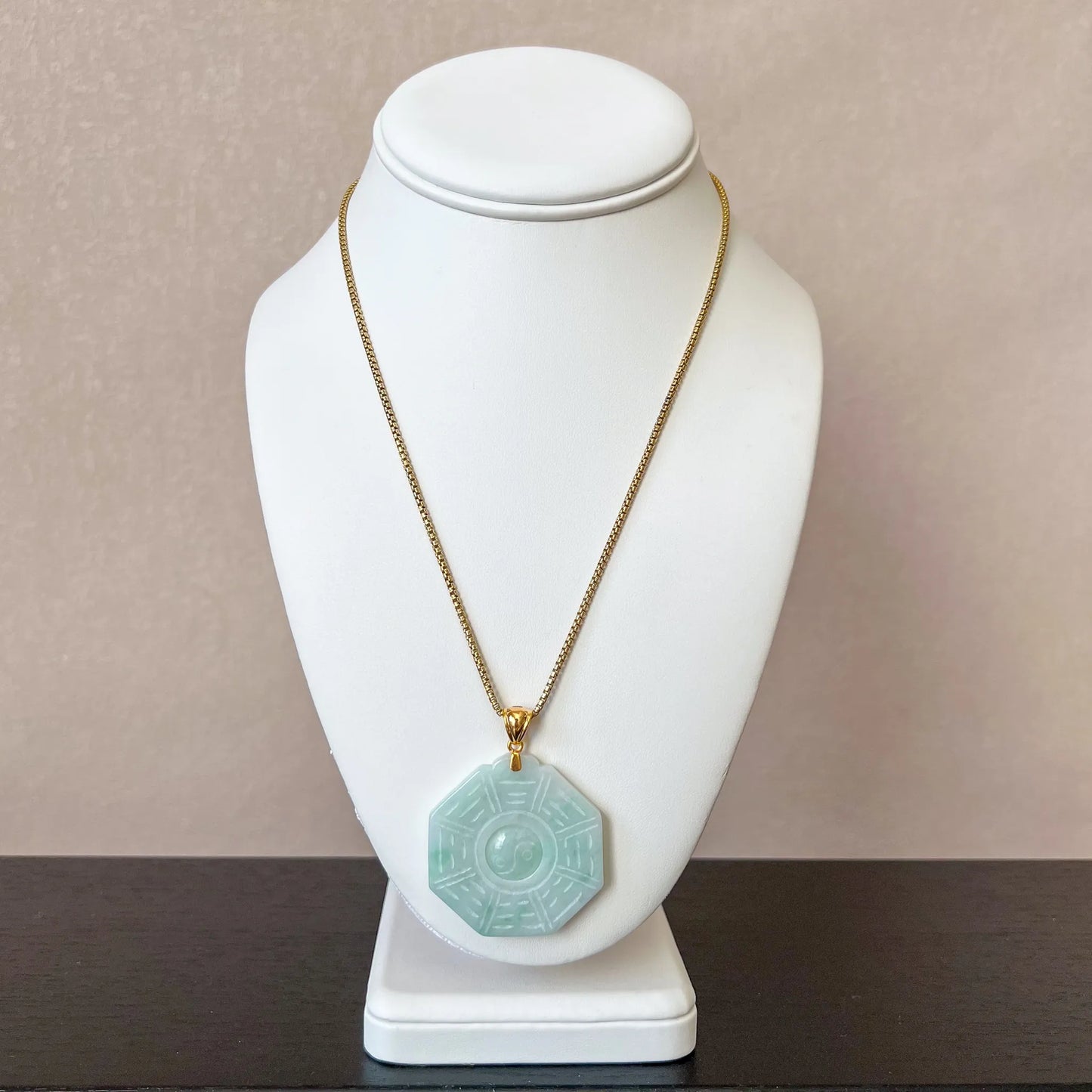 Necklace pendant styled on a white bust display with fine gold chain