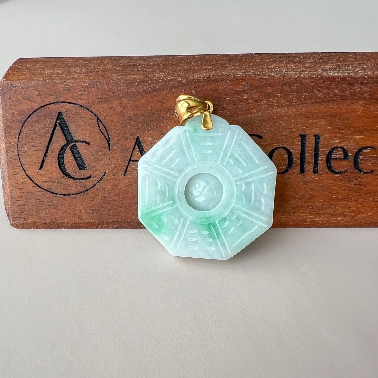 Front view of carved pale green jade pendant on wood display with gold bail